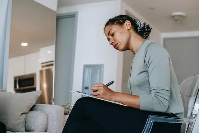 A Black therapist taking progress notes on her clipboard while seated in front of a patient.