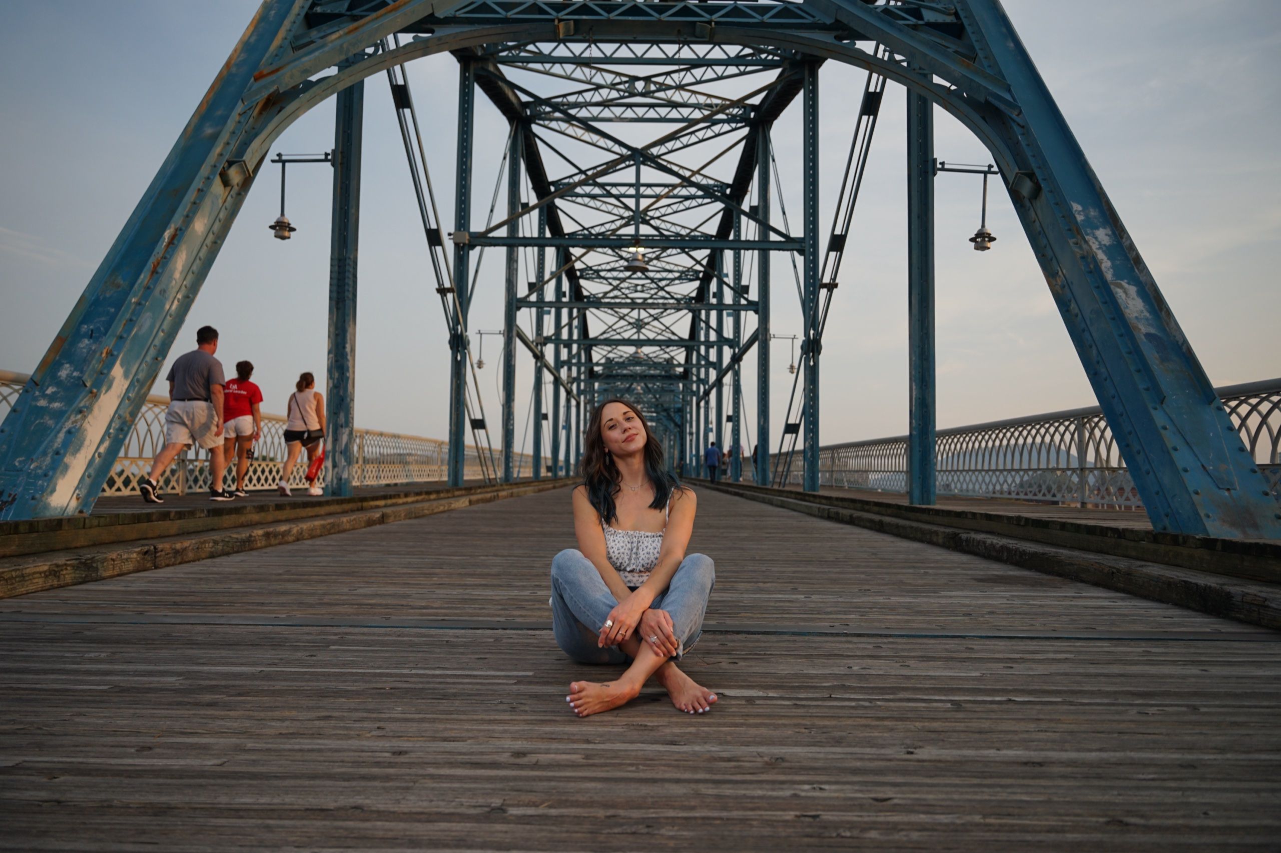 Seated portrait on the wooden deck of the Walnut Street Bridge, blue trusses receding into evening light
