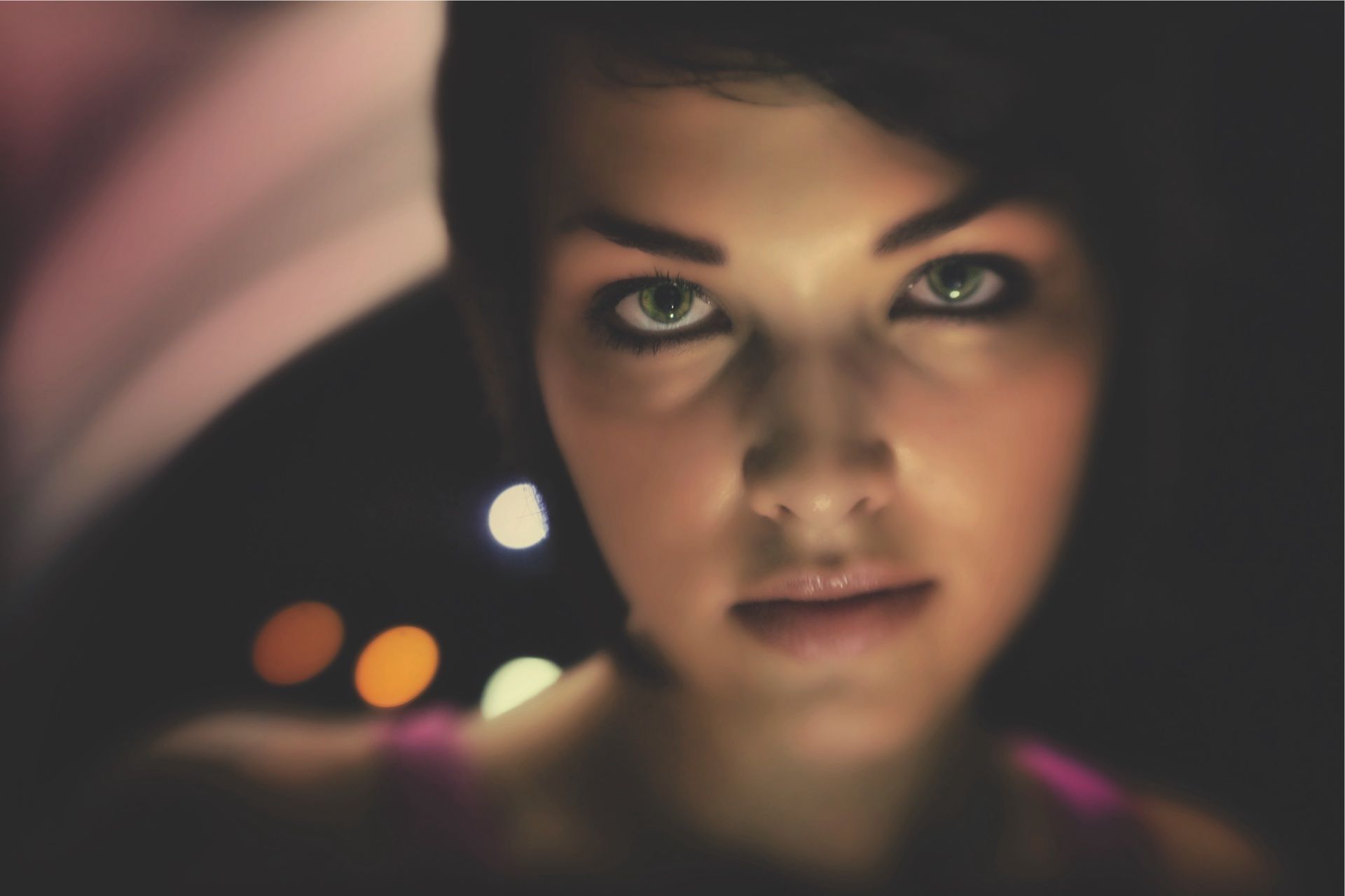 Night close-up — green eyes catching the light against dark street bokeh