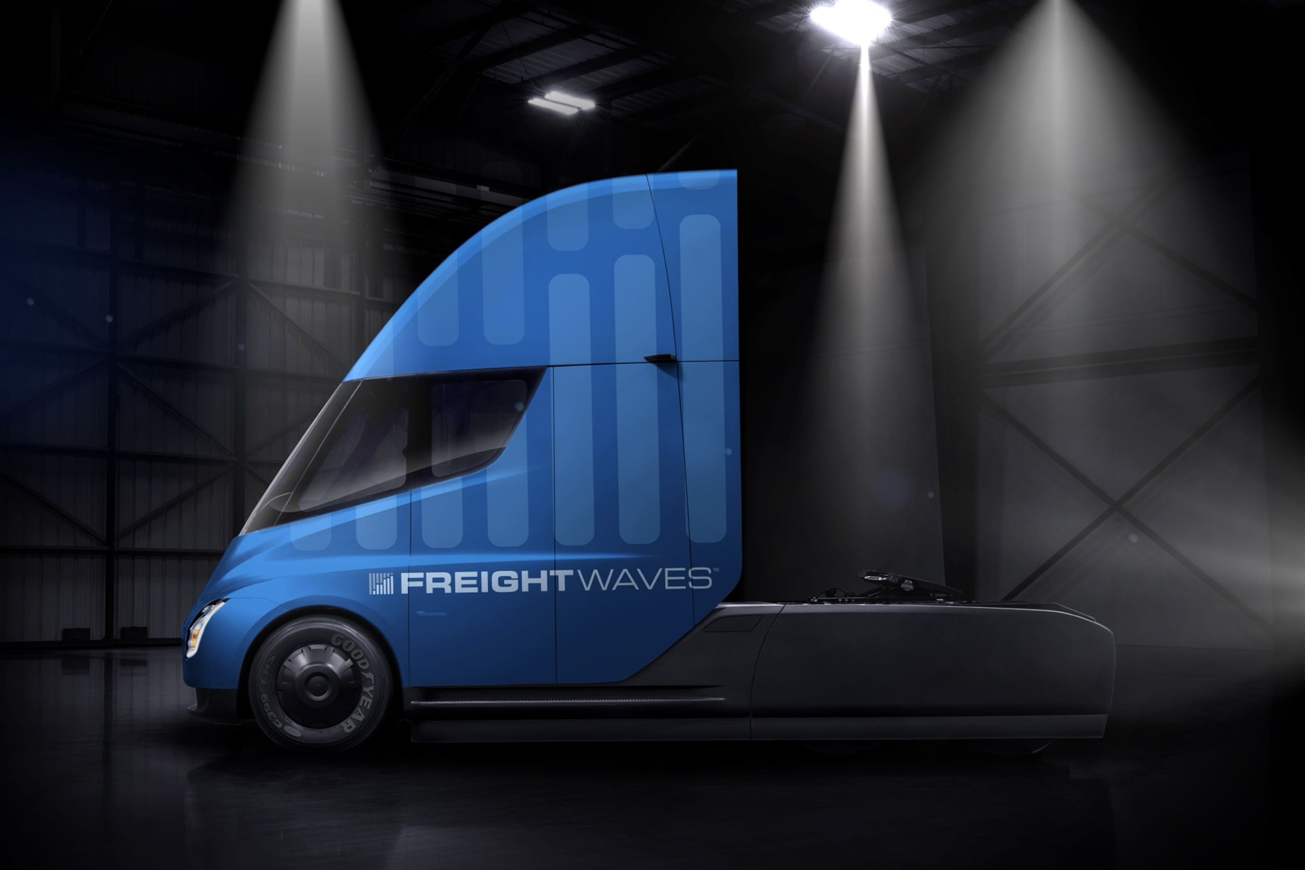 Tesla Semi wrapped in the FreightWaves bar-chart pattern under warehouse spotlights