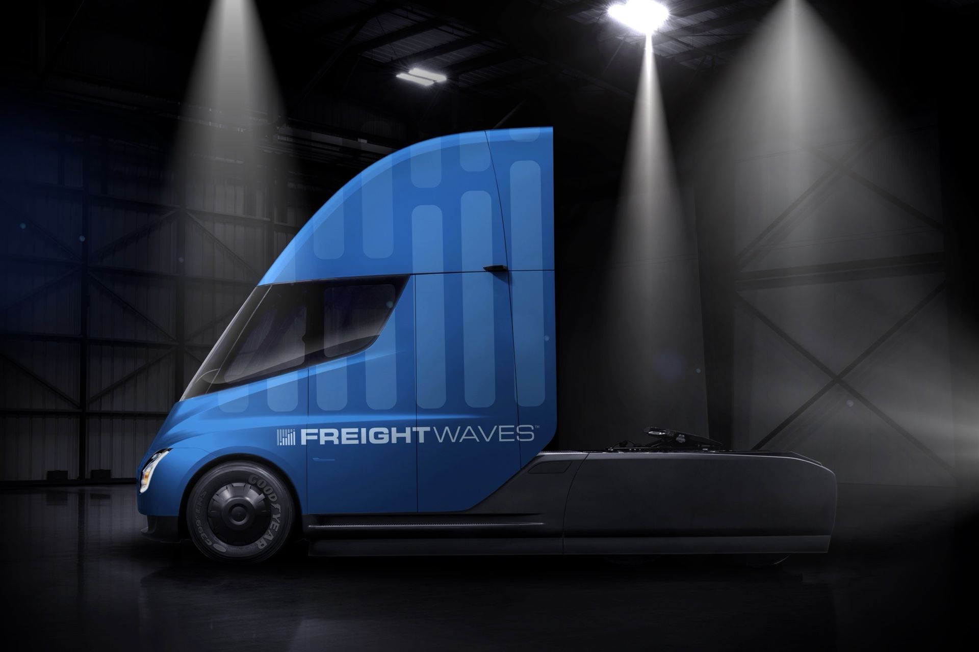 Tesla Semi wrapped in the FreightWaves bar-chart pattern under warehouse spotlights
