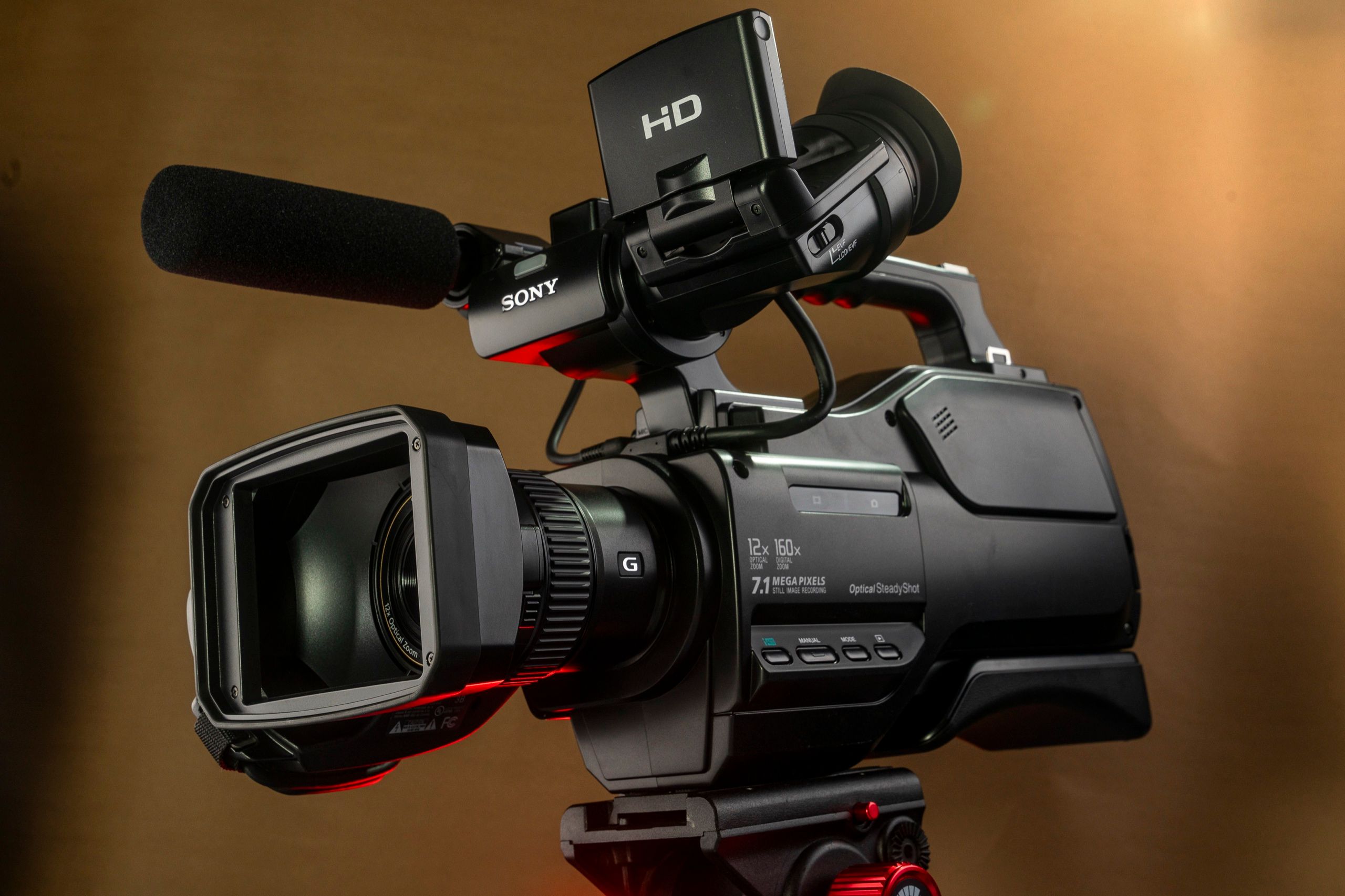 Sony professional camcorder on a tripod against a warm tan backdrop
