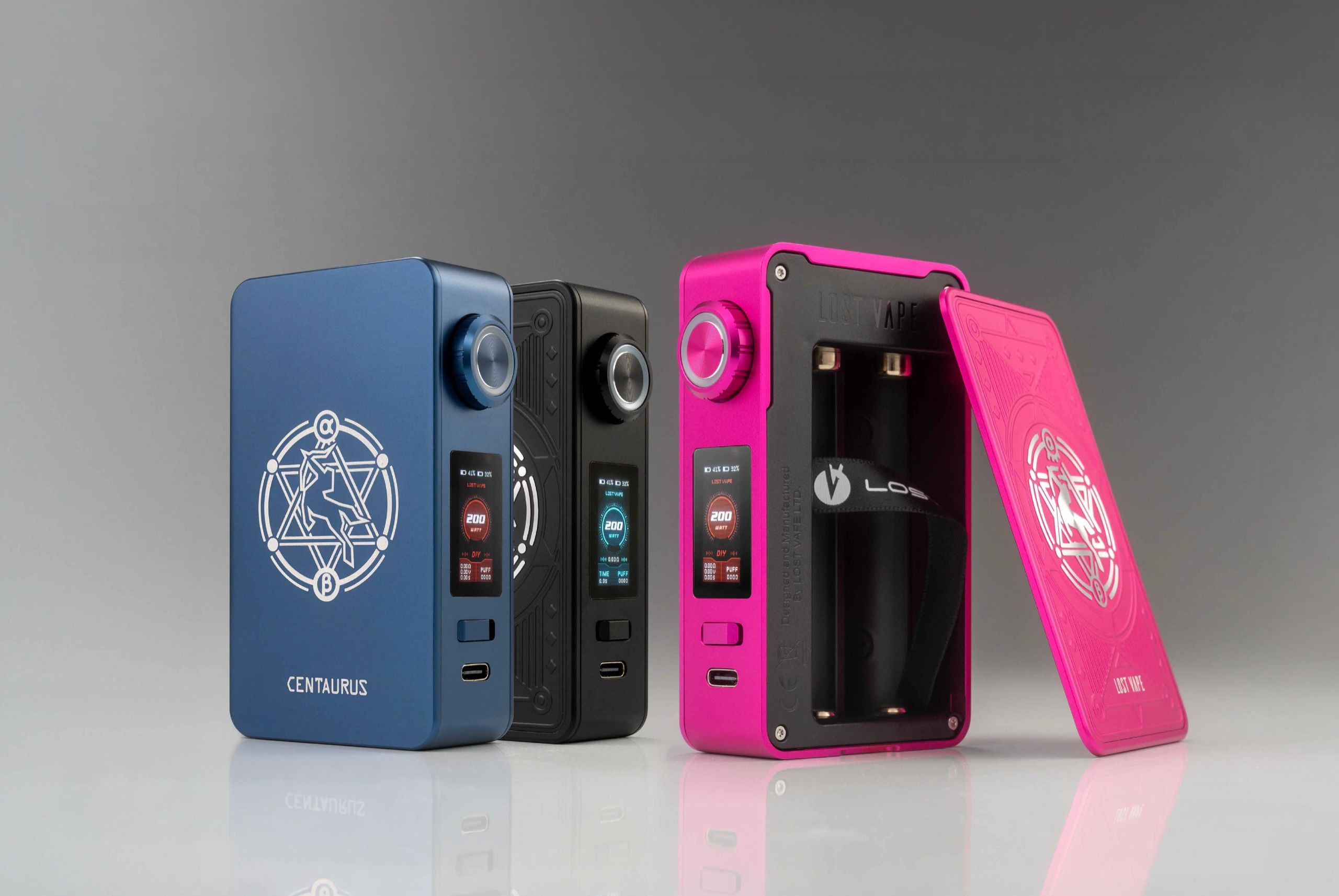 Lost Vape Centaurus mods in blue, black, and pink, one opened to its battery bay, on gray seamless