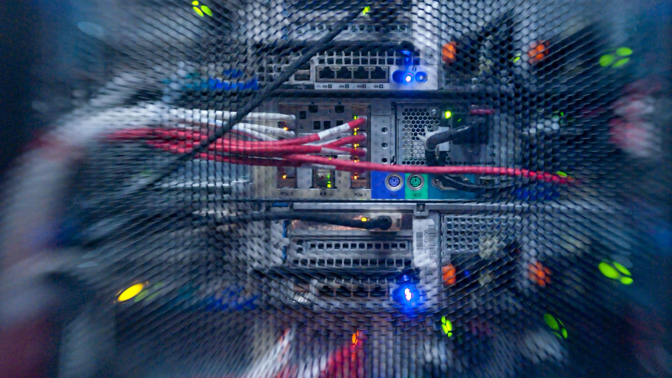Server rack detail through mesh — colorful cabling and LEDs in soft focus