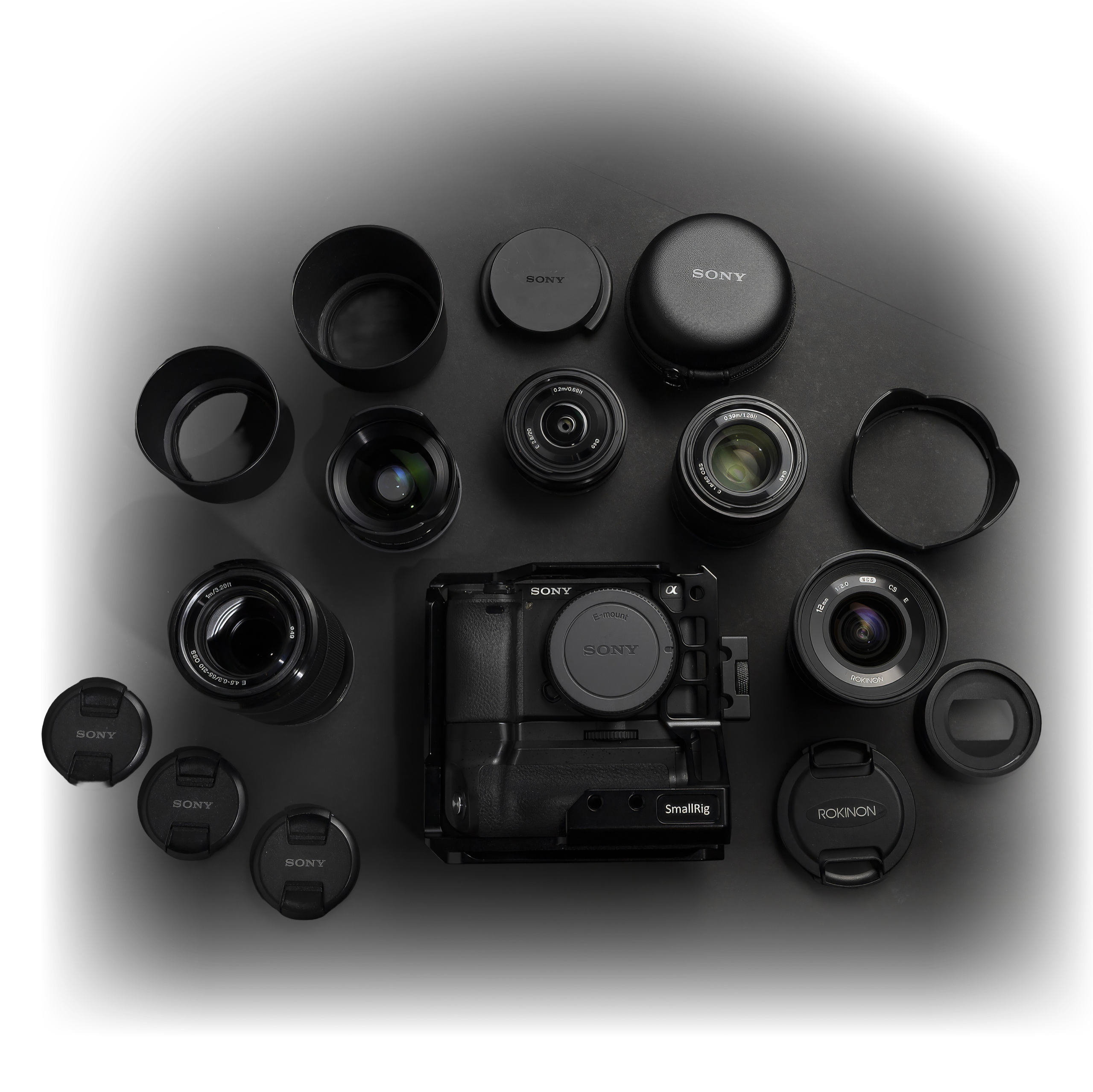 Sony a6300 kit laid out flat on black — the caged body ringed by lenses, hoods, and caps