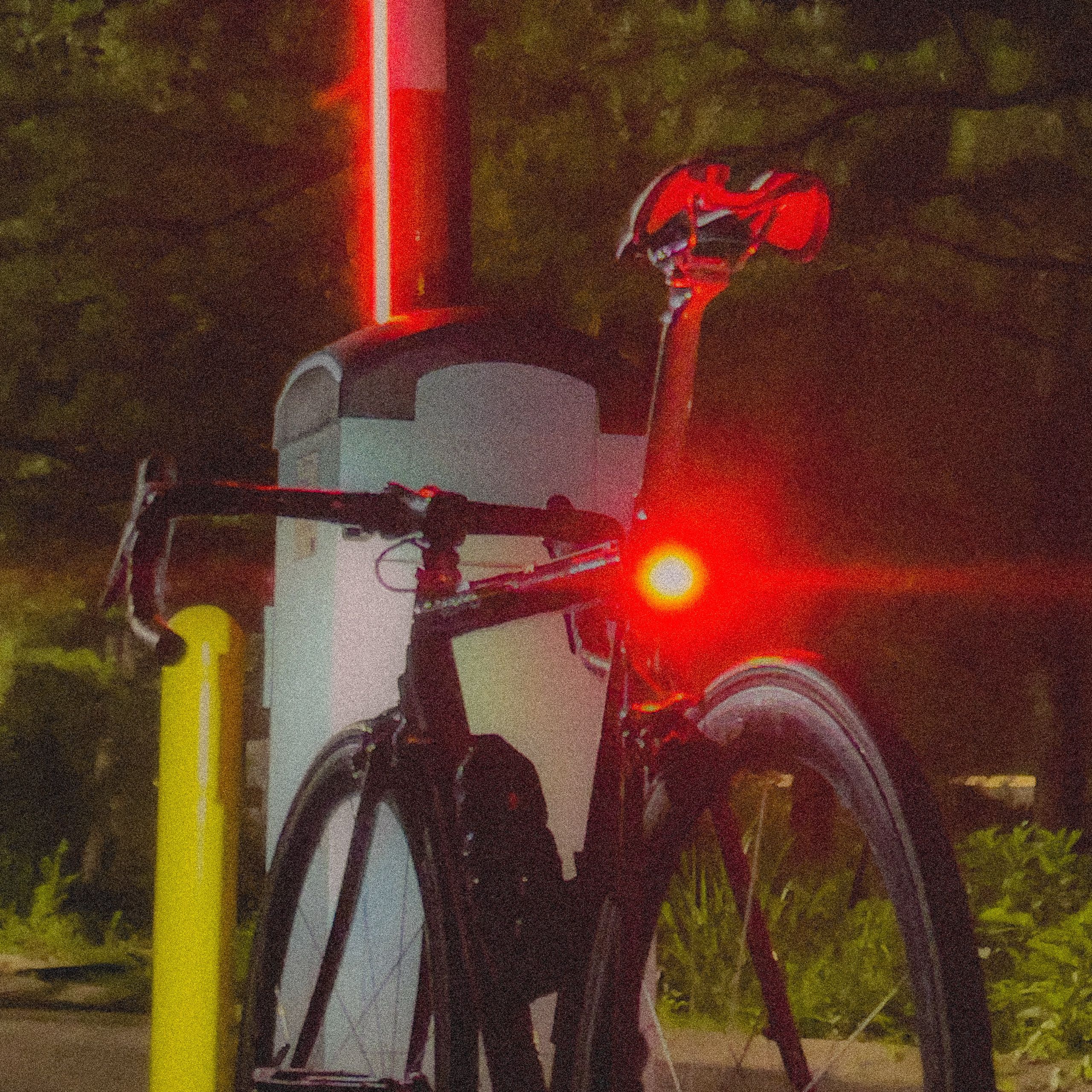 Road bike parked against a bollard at night, its rear light burning red