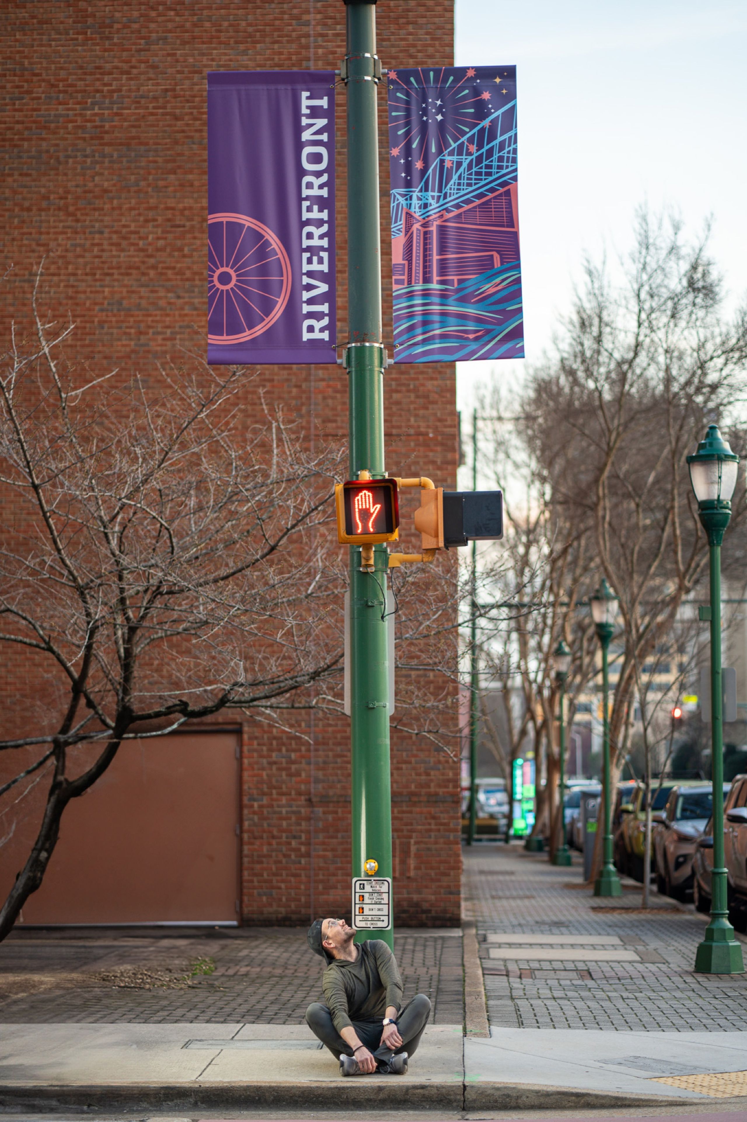 Riverfront banners installed on a signal pole downtown — a passerby seated on the curb looking up