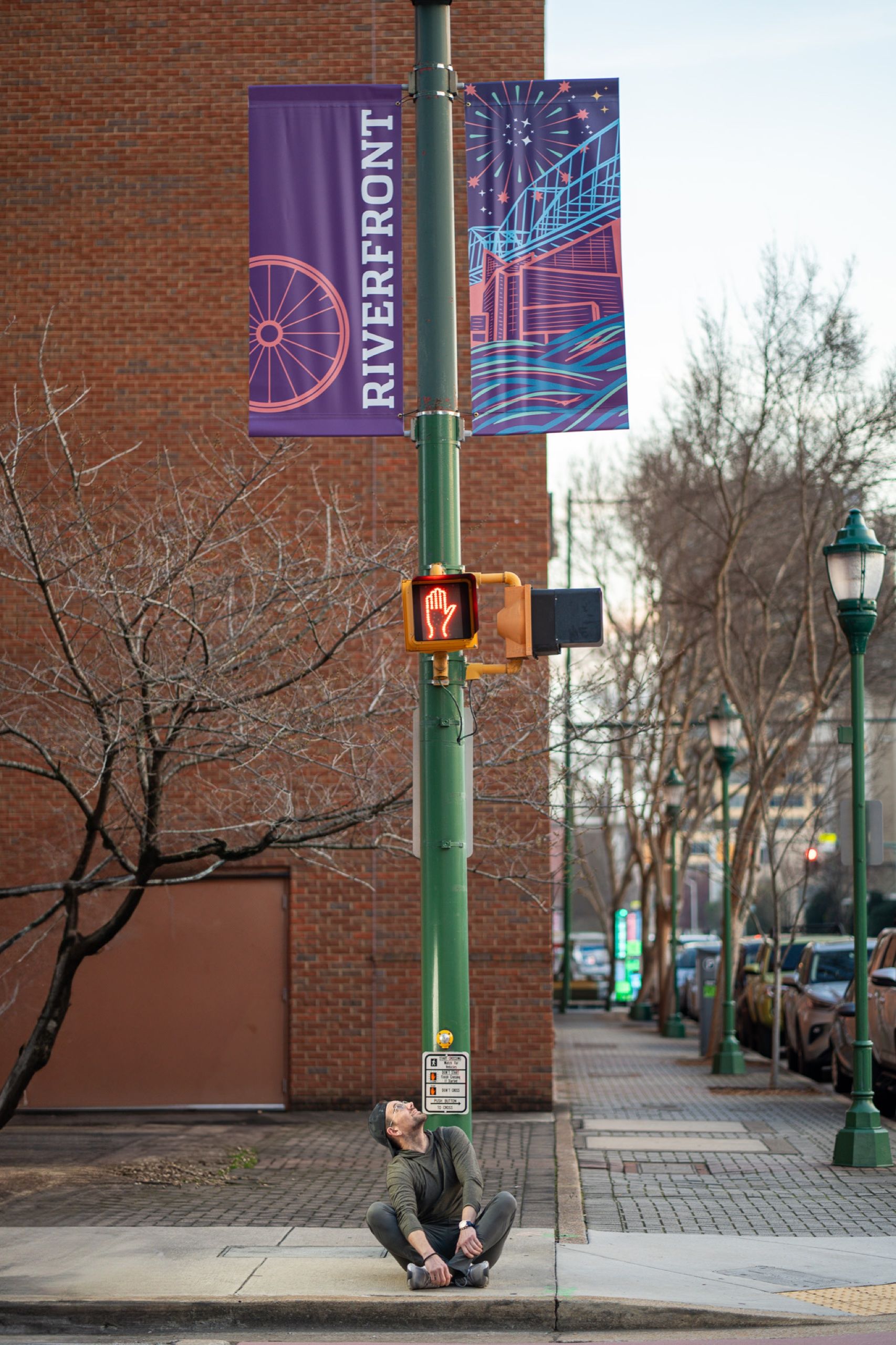Riverfront banners installed on a signal pole downtown — a passerby seated on the curb looking up