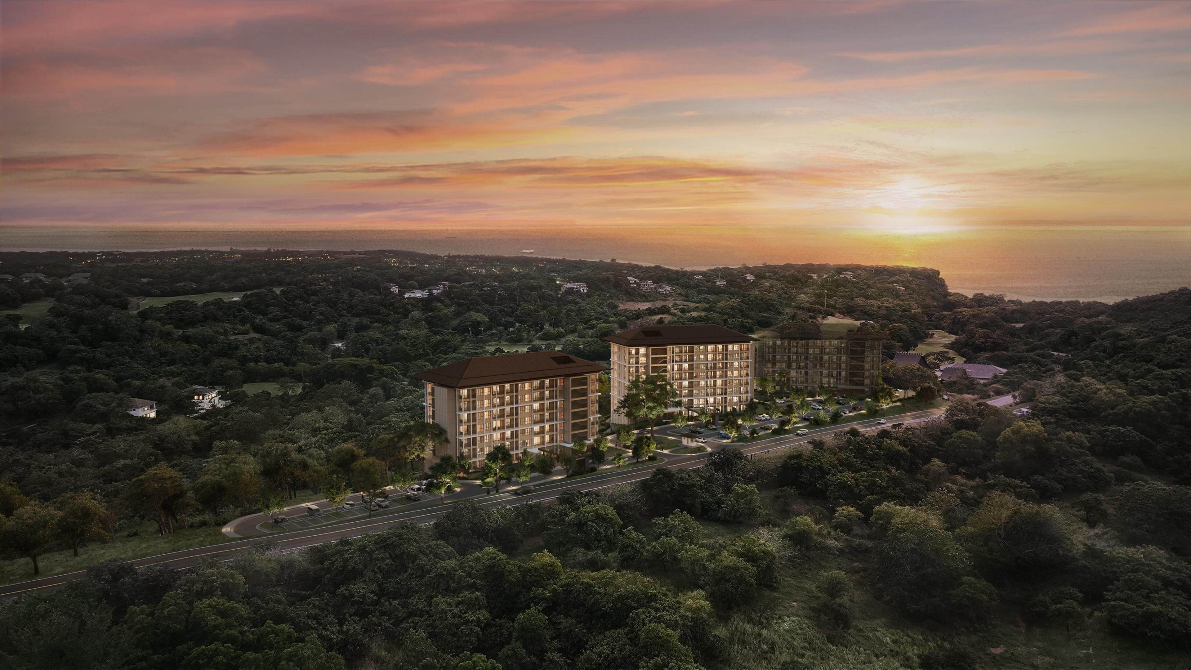Aerial render of Searidge Residences at Anvaya Cove at sunset, mid-rise buildings nestled in forested hills above the West Philippine Sea