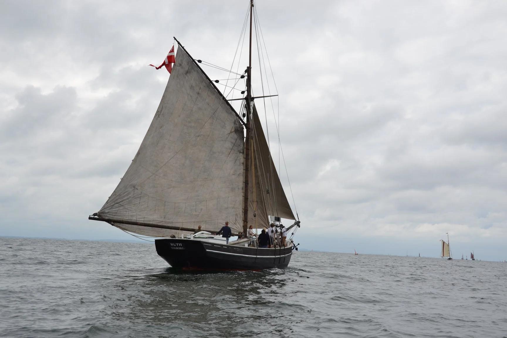 Sejlbåd med flere personer sejler på havet under en overskyet himmel