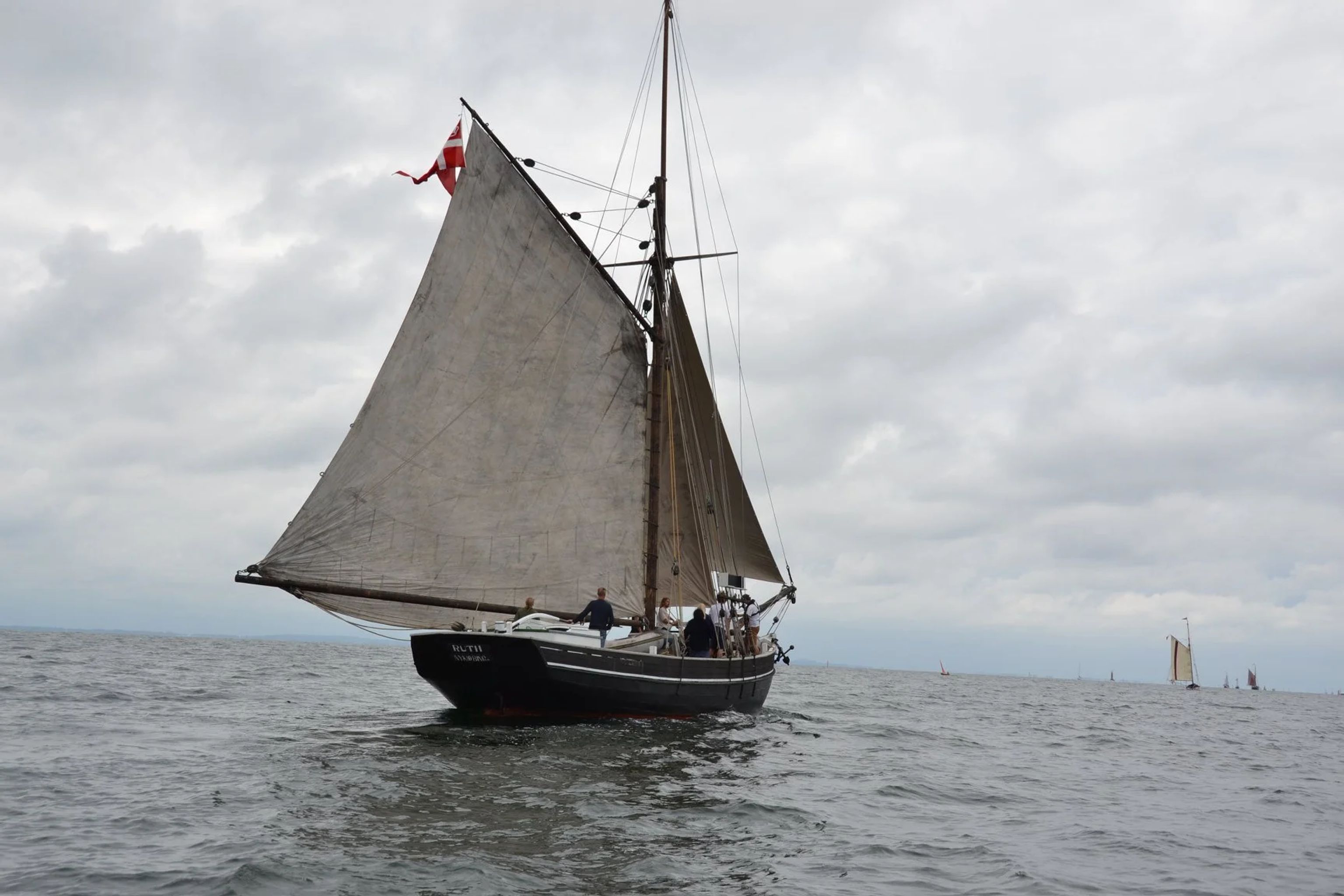 Sejlbåd med flere personer sejler på havet under en overskyet himmel