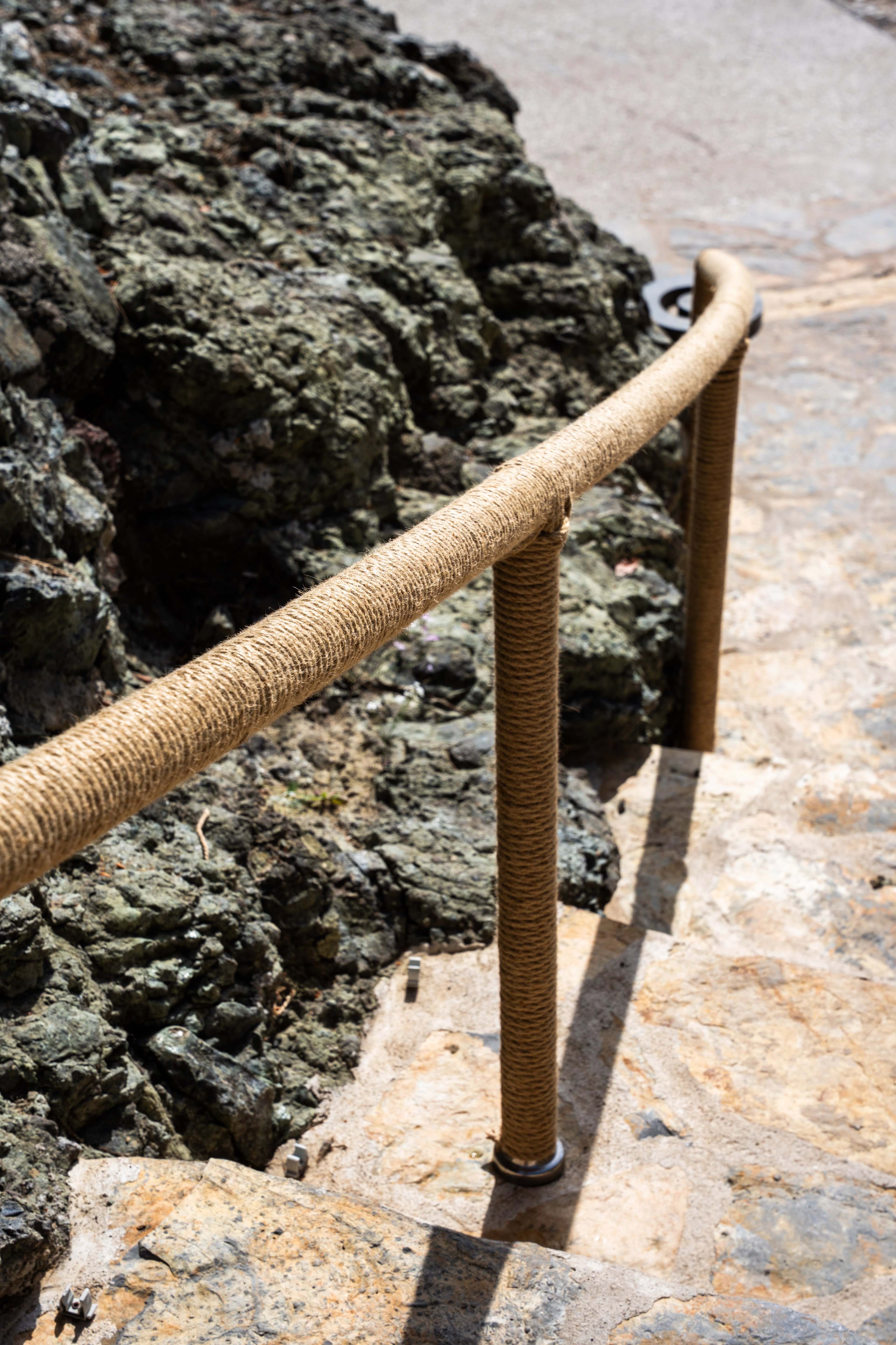 Close view of a rope-covered rail curving beside rocks and a stone path at NG Phaselis Bay.