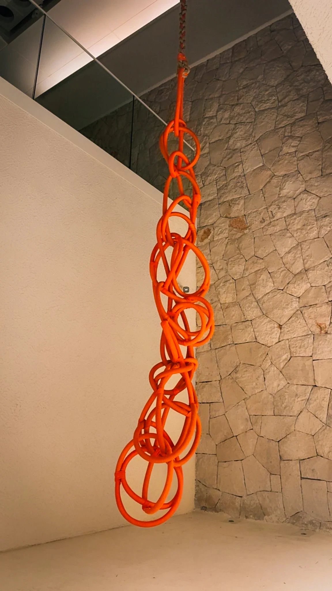 Karma, a sculpture of orange rope loops hanging beside a stone wall