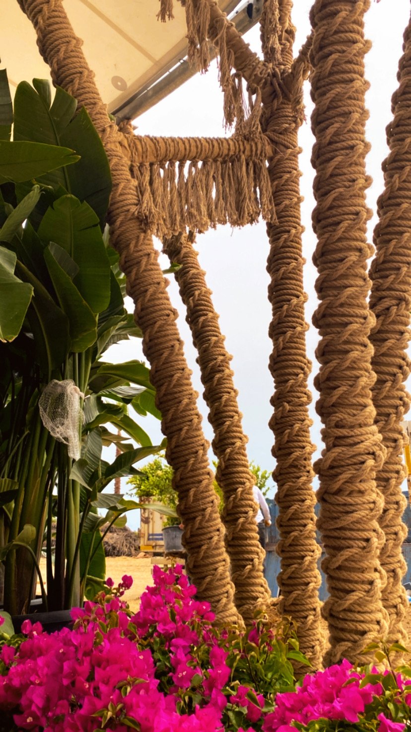 Close view of rope-wrapped posts and horizontal fringe among green leaves and pink bougainvillea at Ethno Hotels Belek.