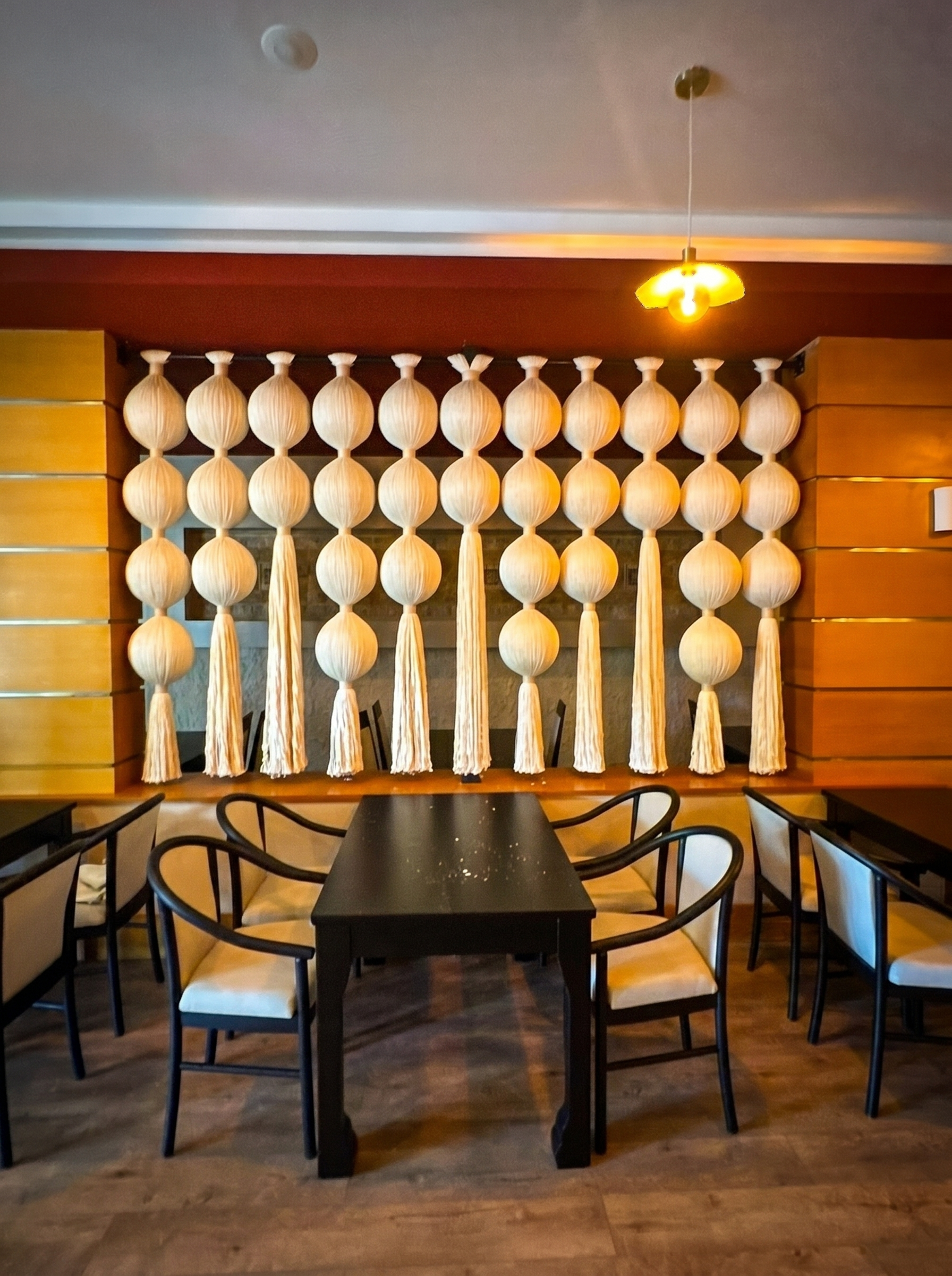 Rows of cream rounded forms and tassels behind a dark dining table at MC Arancia Resort Hotel.