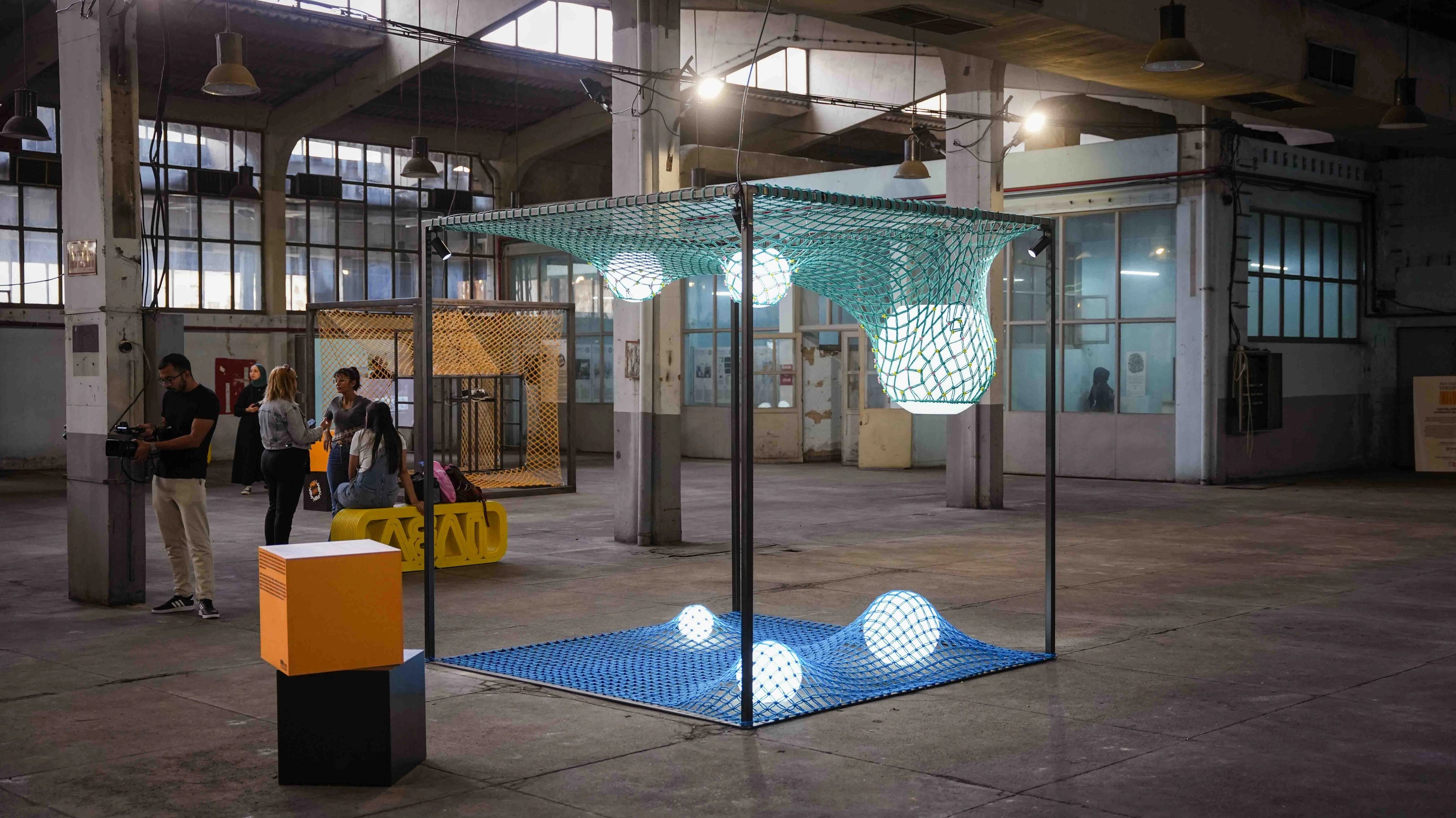 An installation of teal overhead netting, blue floor netting and illuminated spheres inside a rectangular frame at IABA 2025.