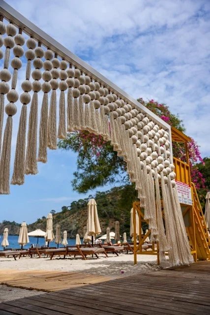 An angled view of a broad cream sphere-and-tassel entrance screen above a beach deck at So Beach.