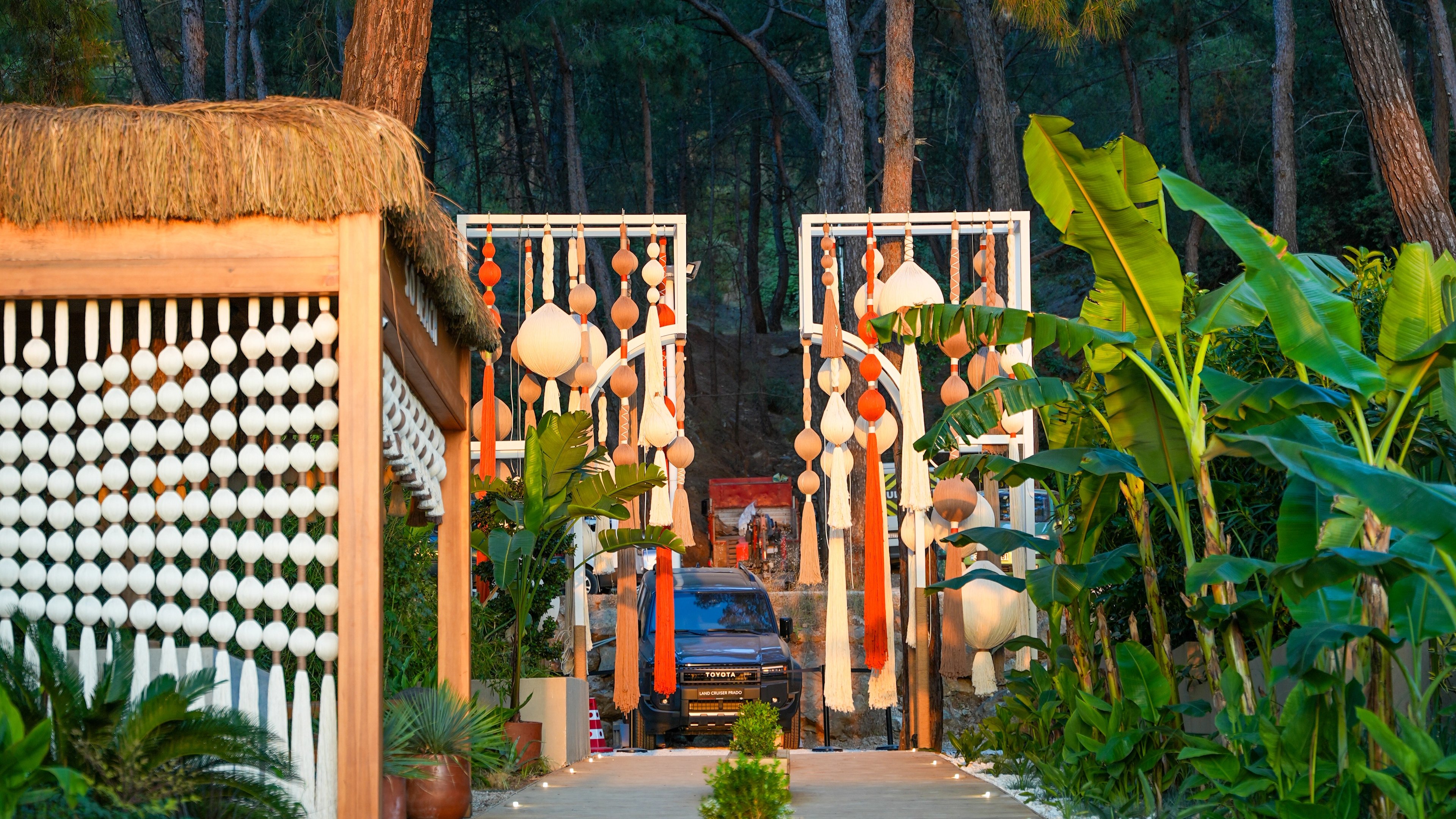 Decorative panels with suspended rounded forms and tassels along an illuminated timber walkway at So Beach.