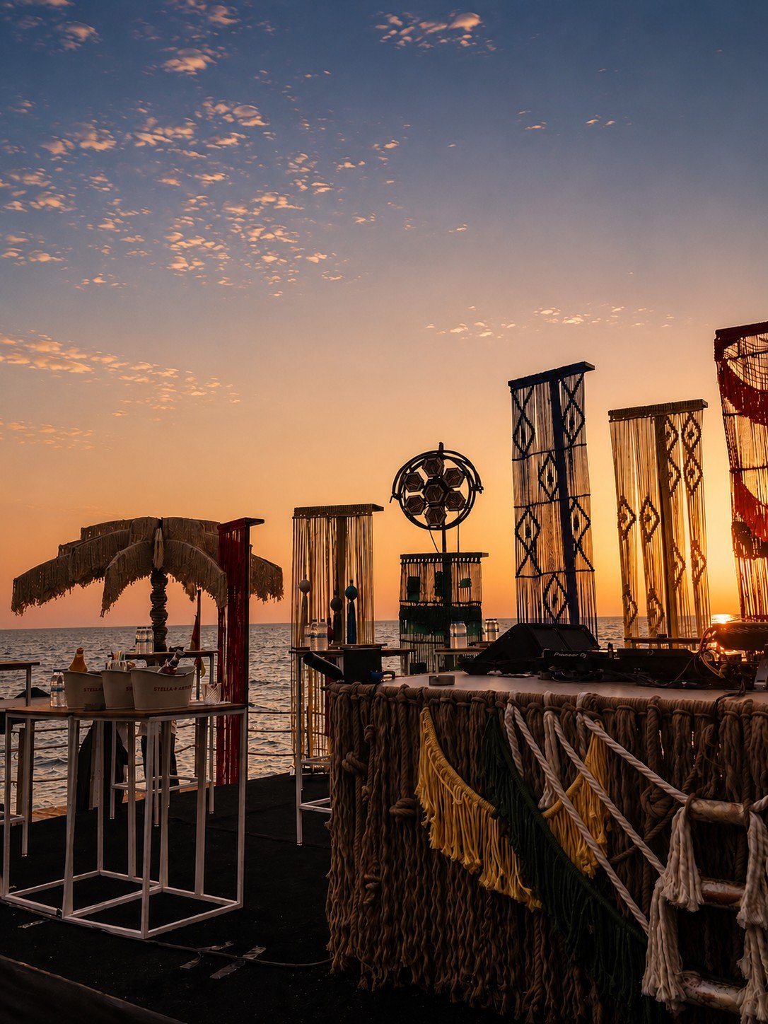 Rope fringe along the front of a waterfront stage, with tall decorative frames and a Dimare Palm Tree at sunset at Bilem Beach.