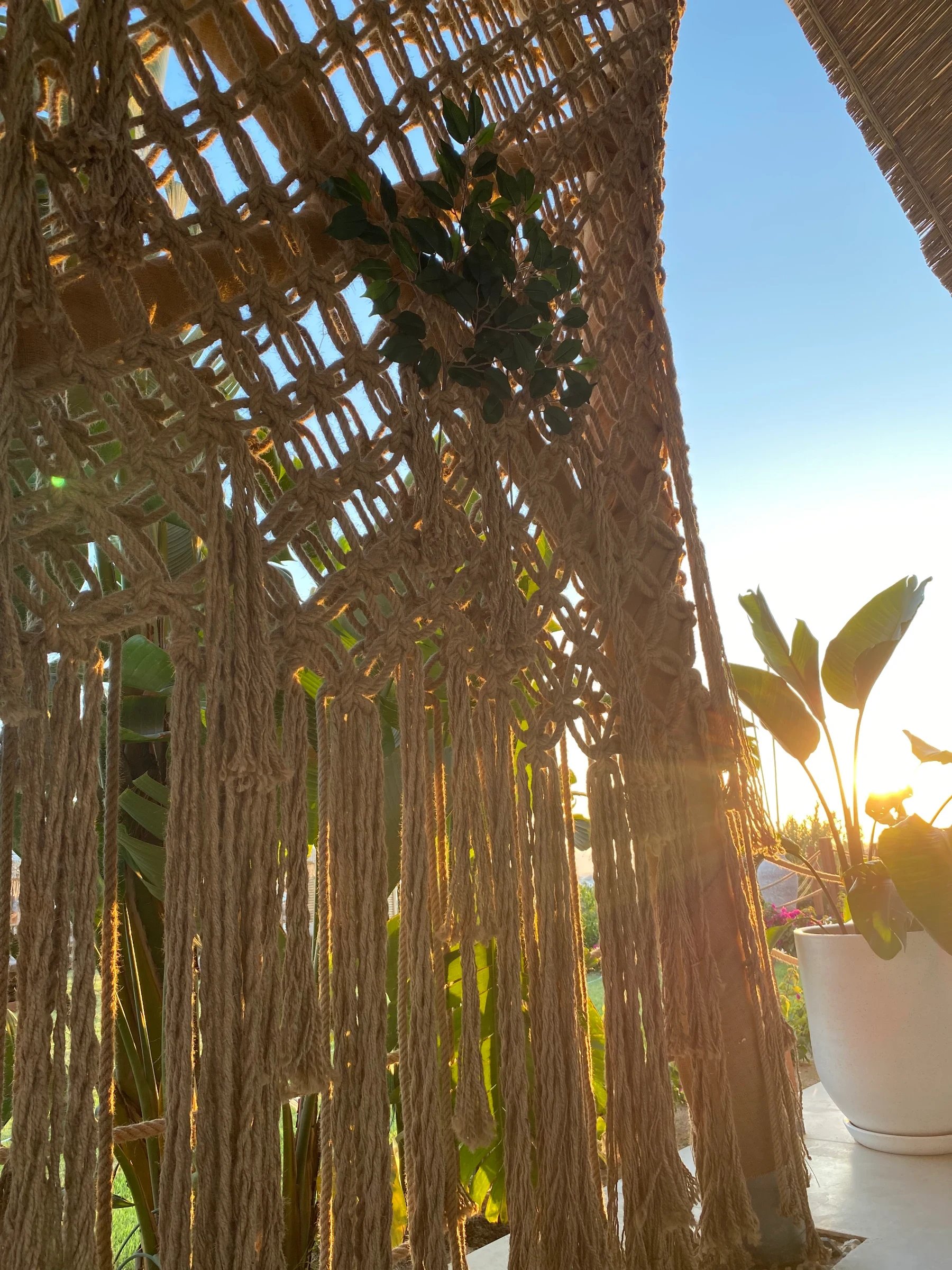 Low sunlight passing through an open knotted rope screen and long fringe beside terrace planting at Ethno Hotels Belek.