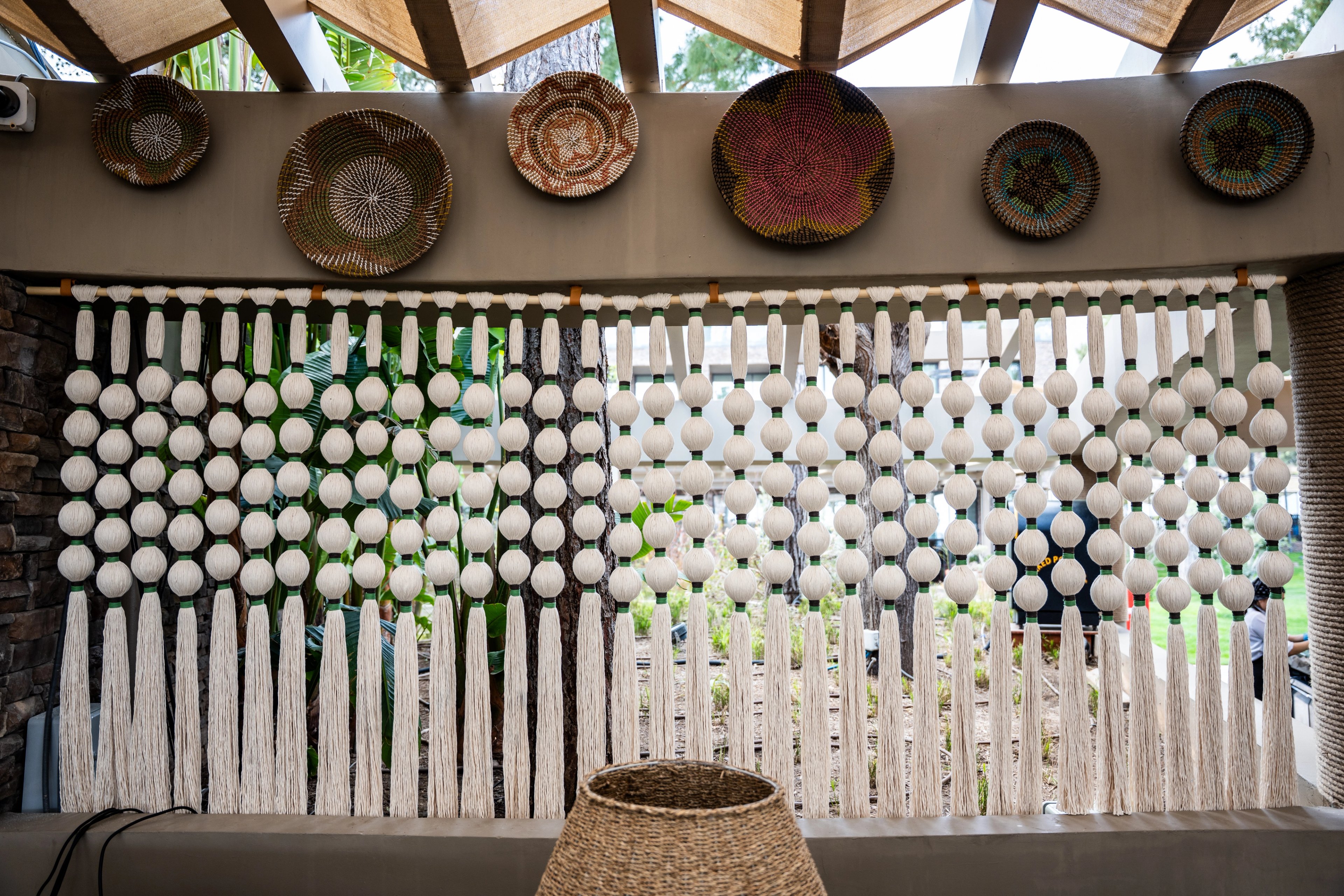 A cream screen of rounded wrapped forms with green bands and long tassels beneath decorative wall plates at NG Phaselis Bay.