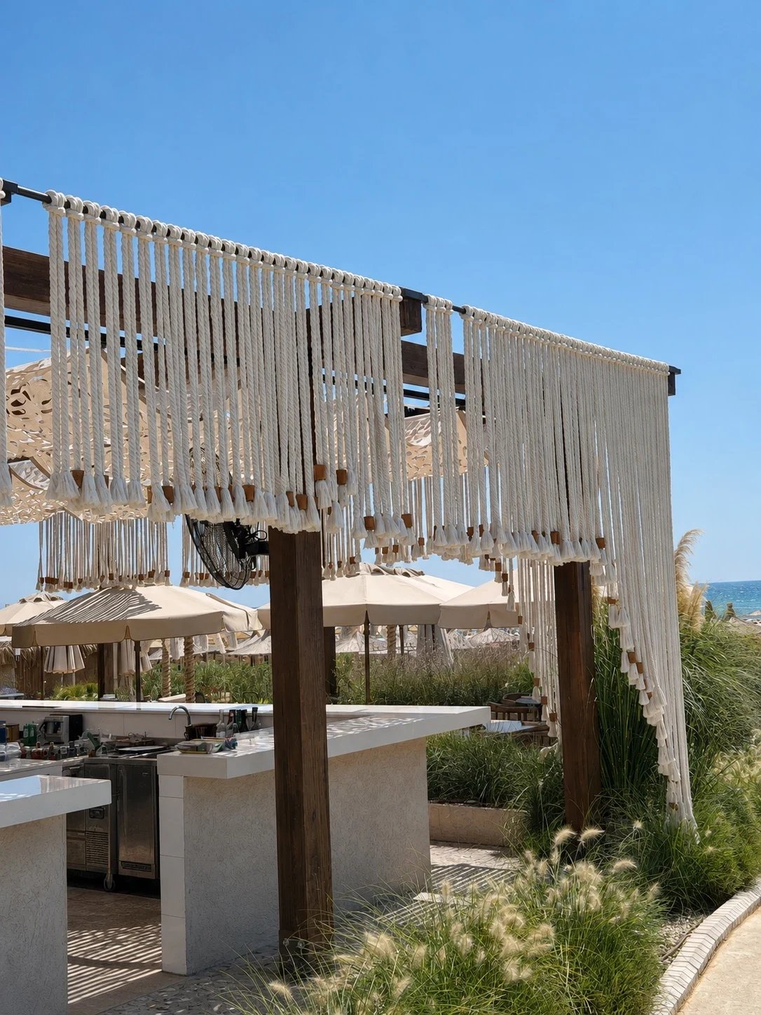 Long rope fringe with wooden beads hung from the beach bar pergola at Adalya Bliss, the sea beyond