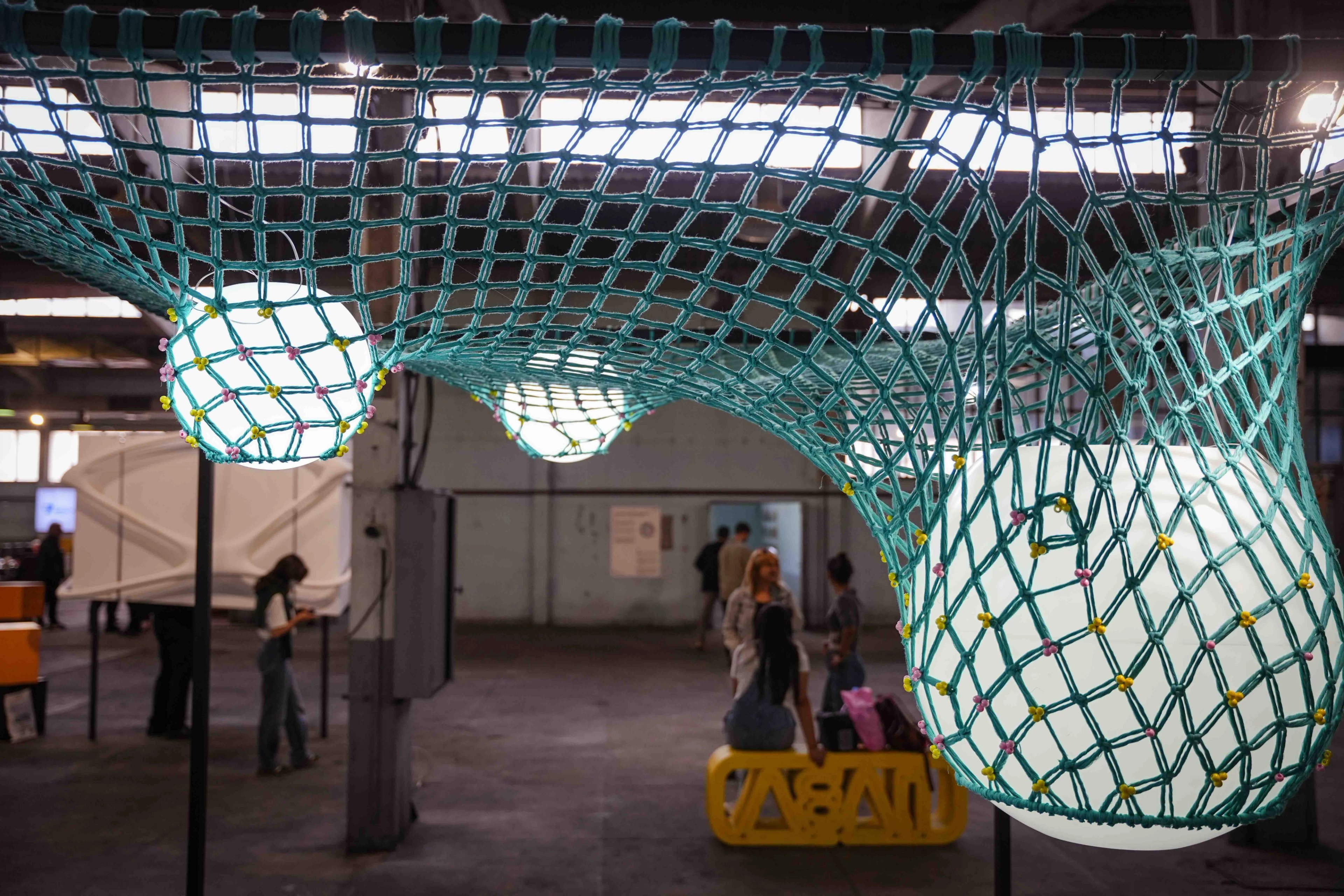 A low-angle view of teal knotted netting curving around illuminated white spheres at IABA 2025.