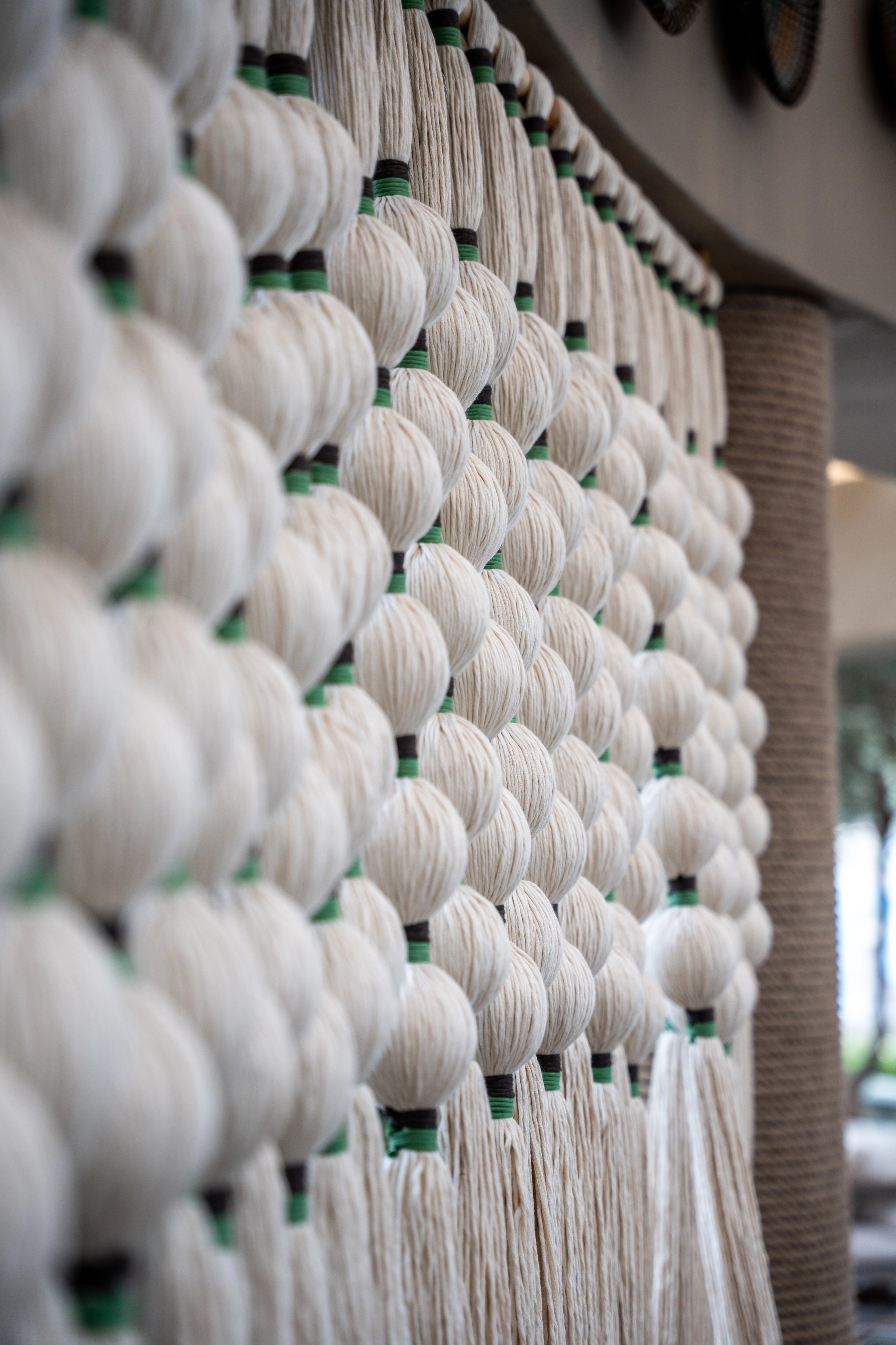 An angled close-up of cream rounded textile forms, green connecting bands and hanging tassels at NG Phaselis Bay.