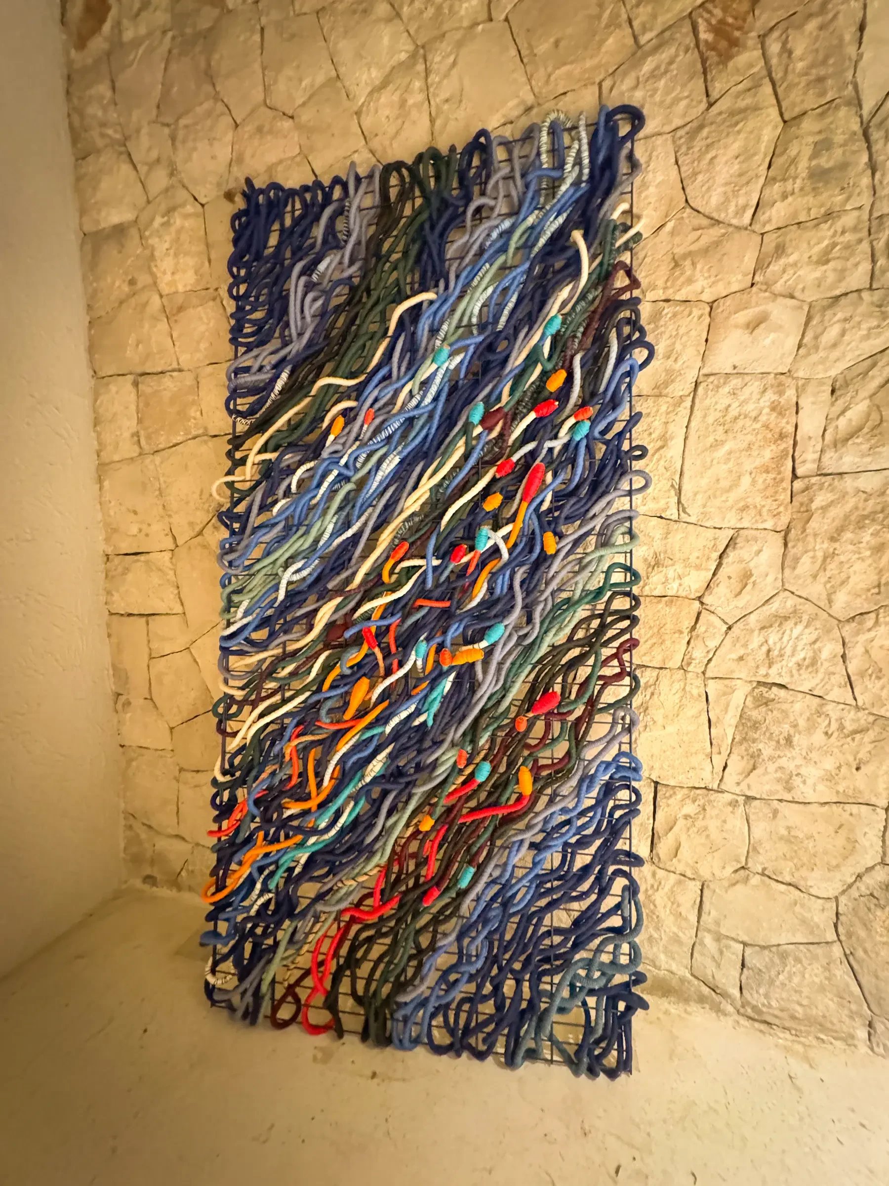 Mavi, a blue hand-woven rope wall piece on a stone wall