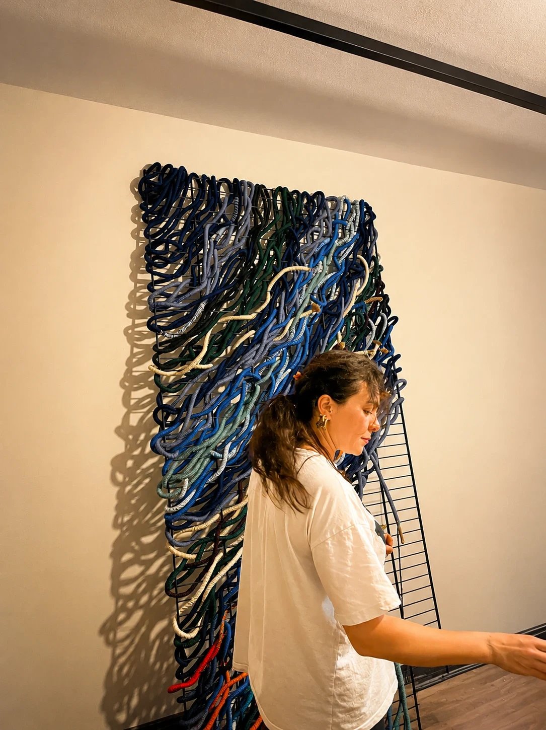 An artisan beside an abstract wall piece made with looping blue and multicoloured cords.