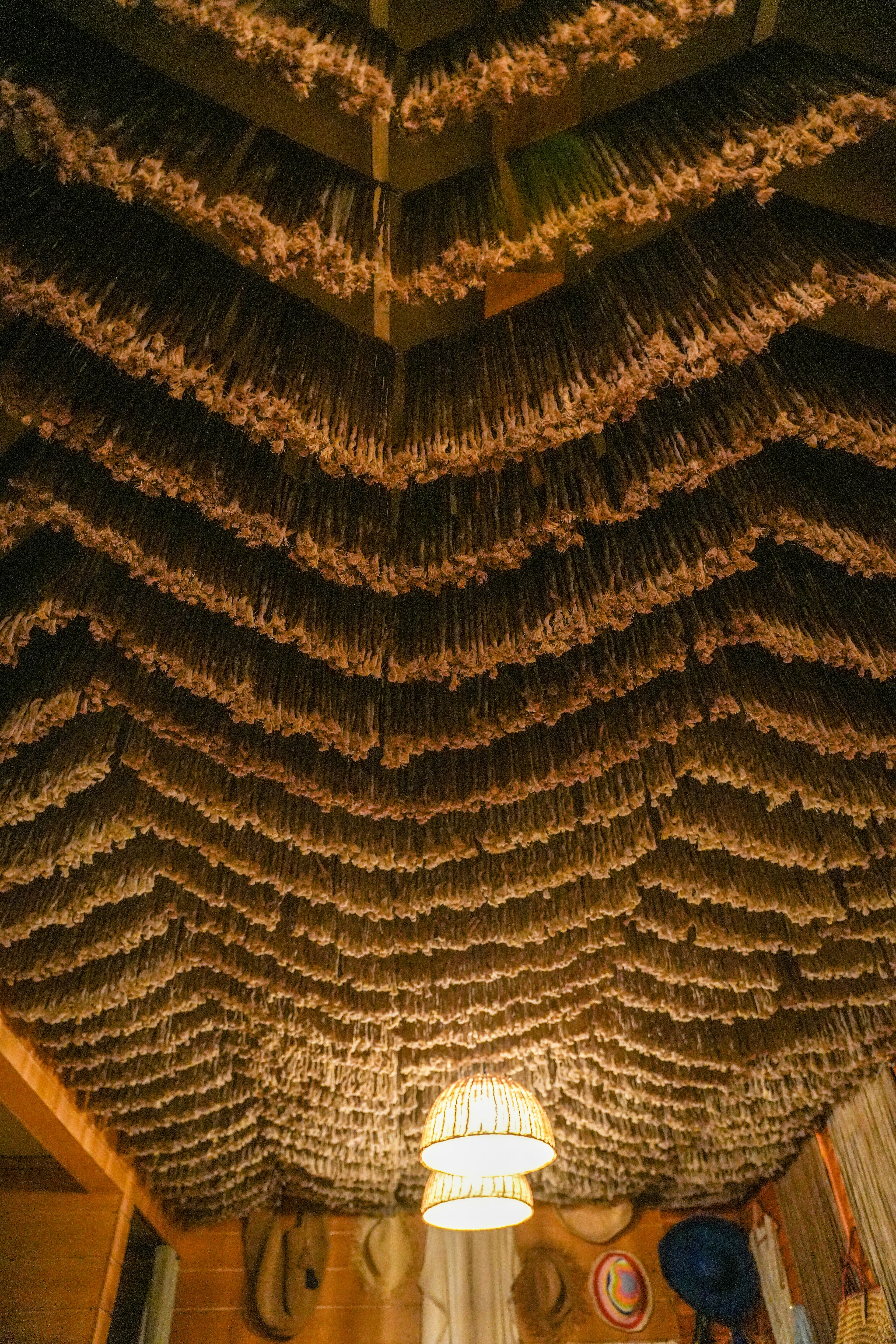 Close upward view of alternating dark and golden fringe rows with a pendant light beneath the canopy at So Beach.