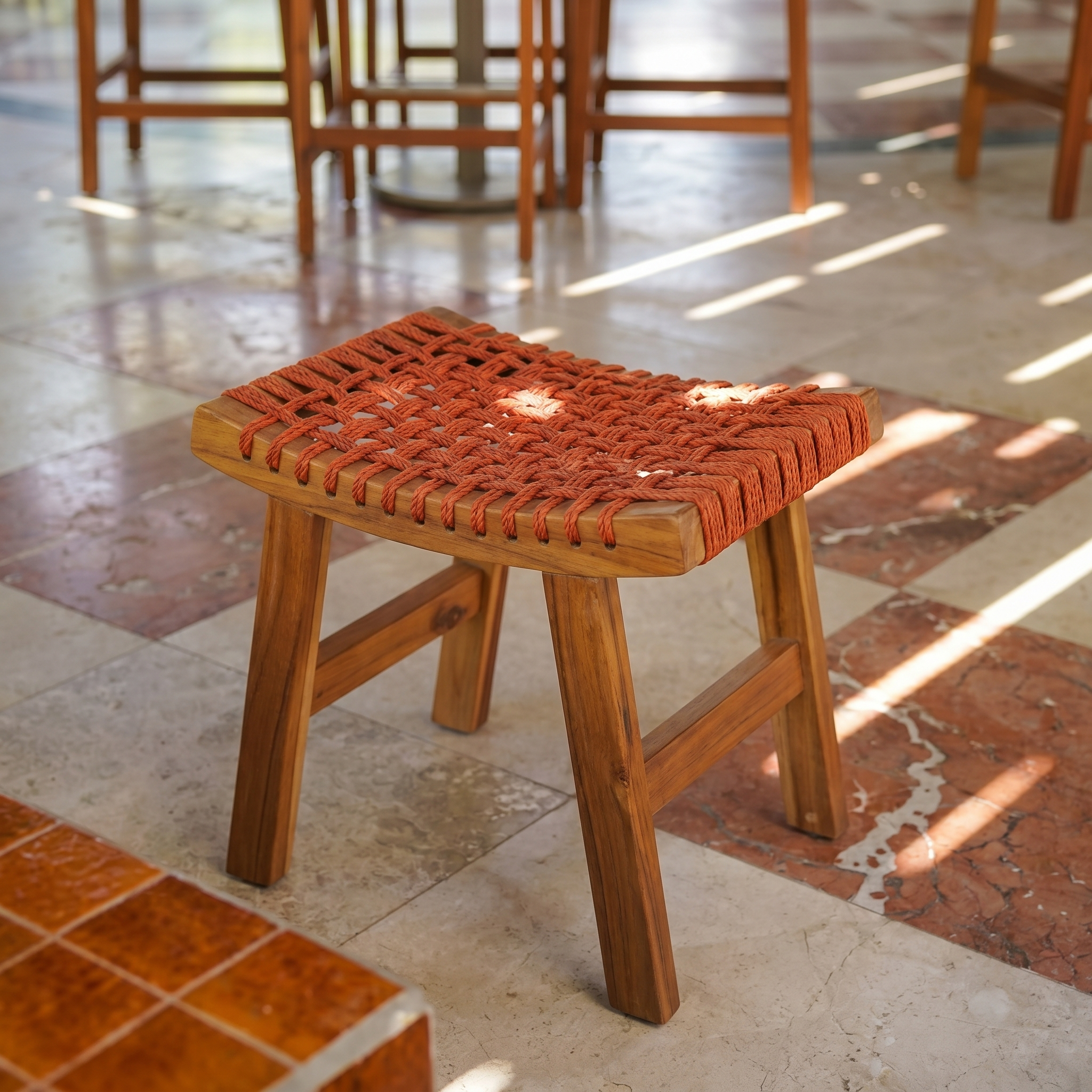 A small timber stool with an orange woven seat in sunlight on a patterned stone floor at MC Arancia Resort Hotel.