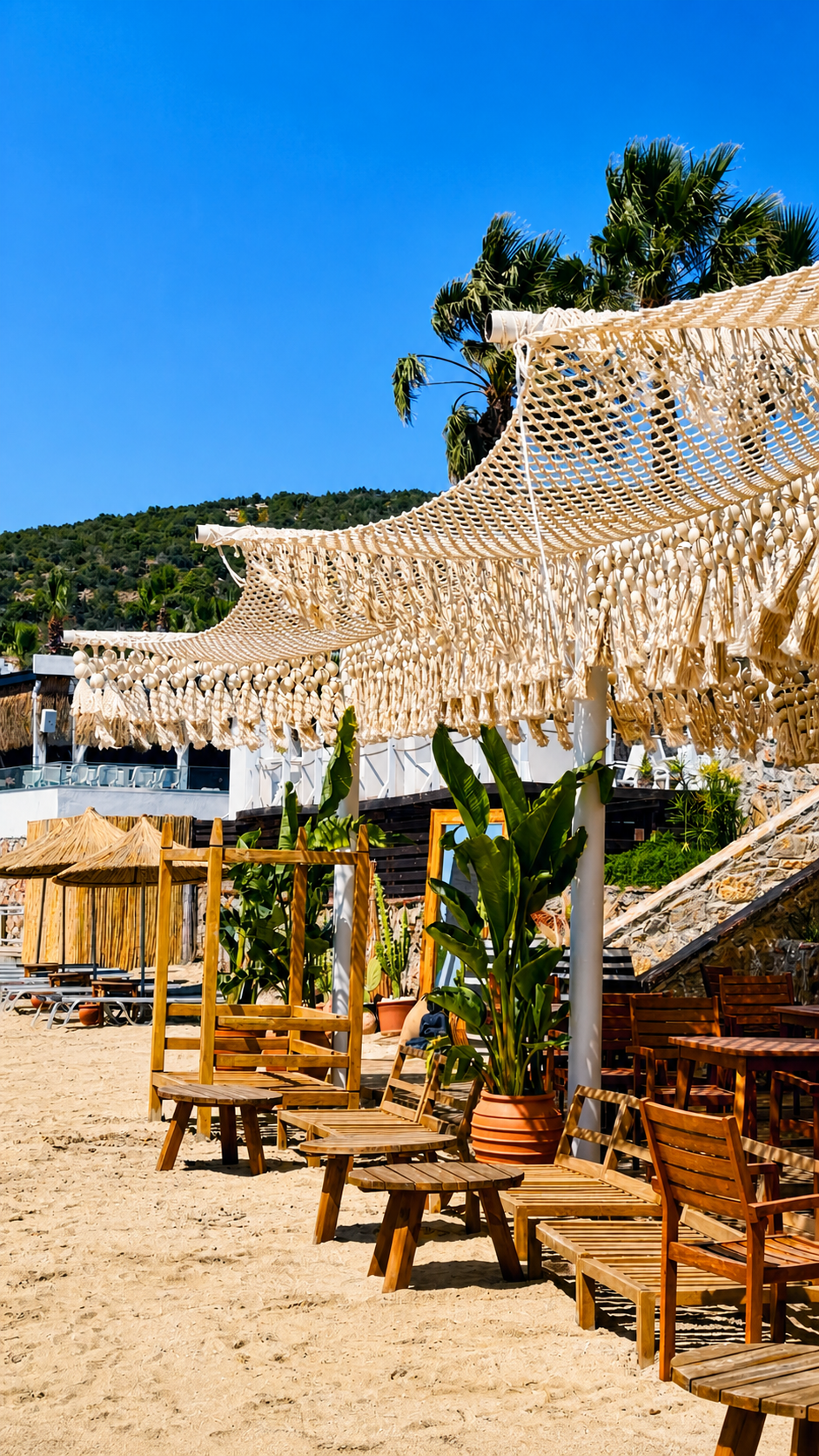 A cream net canopy with hanging fringe above timber tables and chairs on the sand at TUI Magic Life Bodrum.