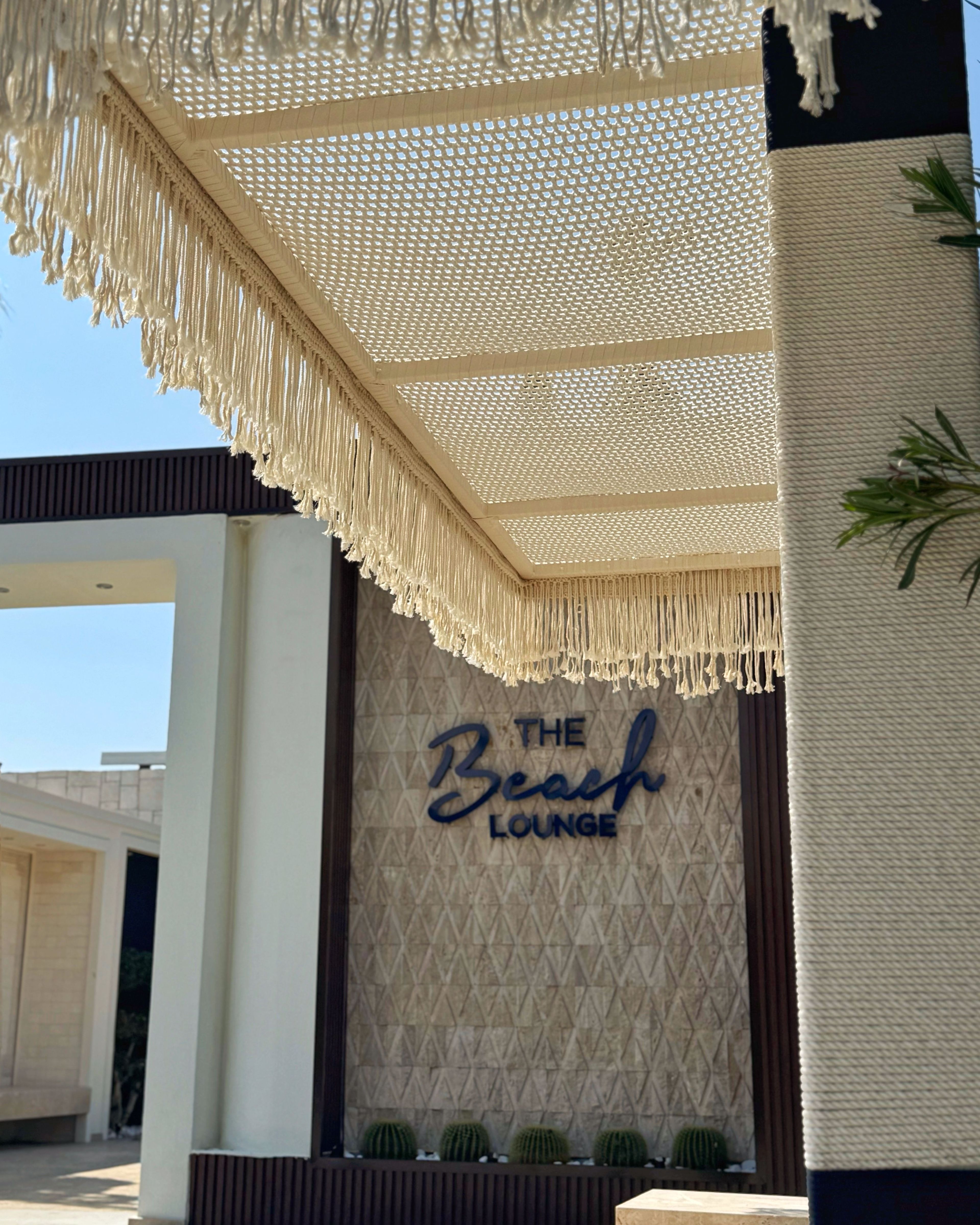 Hand-knotted macramé ceiling panels with a knotted fringe over a hotel beach lounge entrance