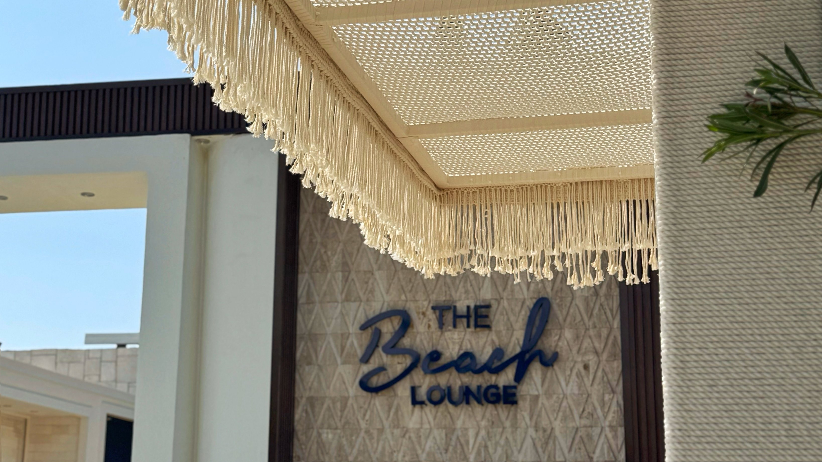 A cream open-weave canopy with a tasseled edge above The Beach Lounge sign at Rixos.