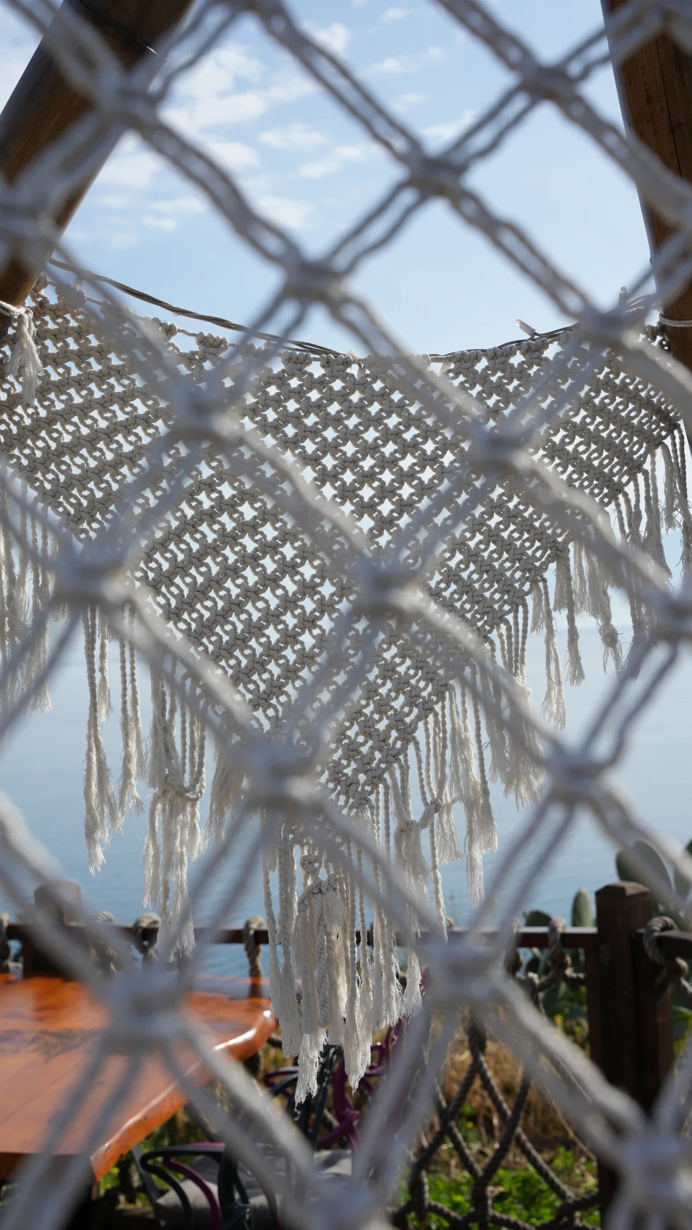 A bamboo A-frame hung with Dimare macramé netting and a fringed panel, open to the sea at Lucky Monkey Hotel
