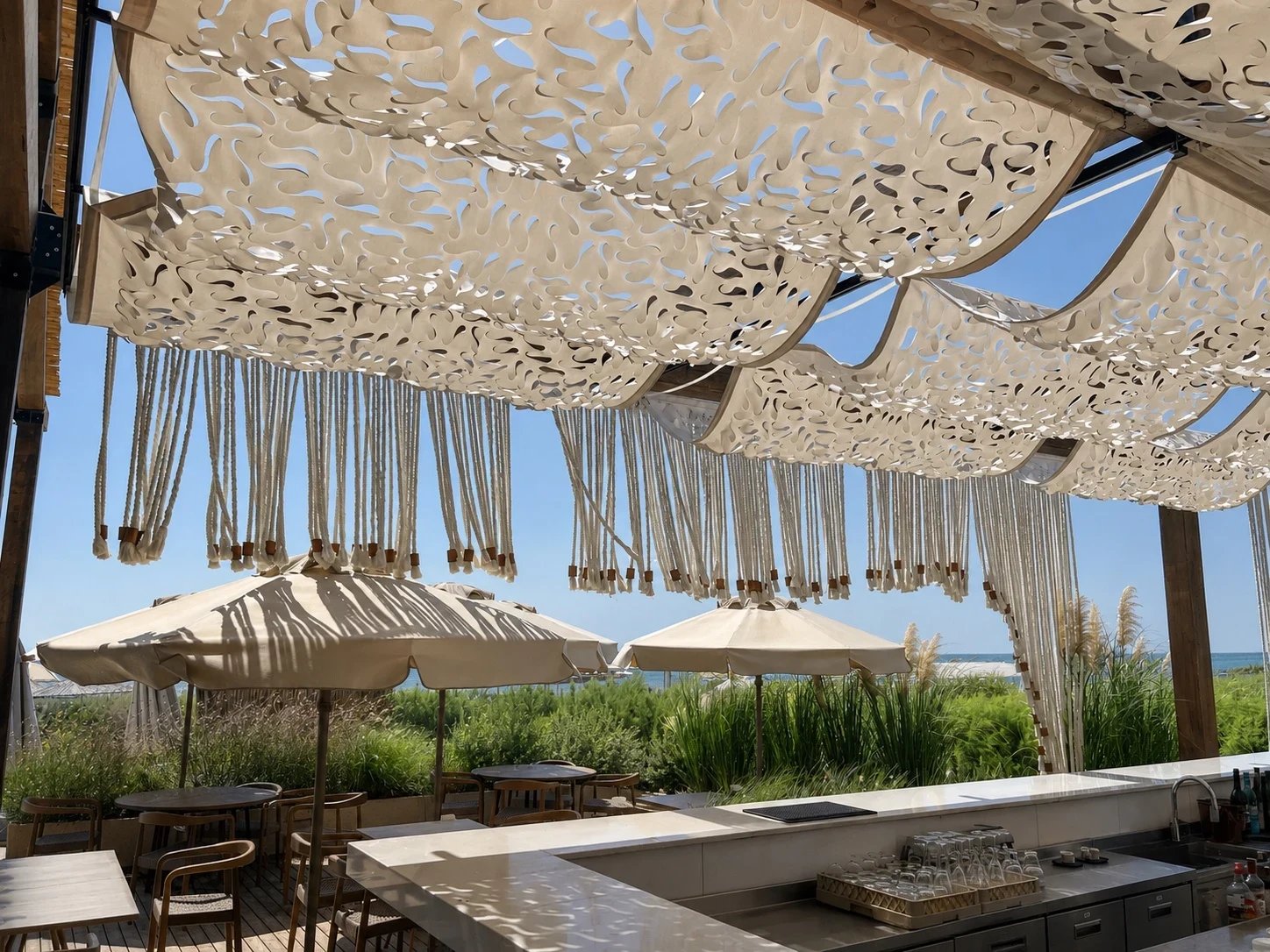 The cut-pattern shade canopy and beaded rope fringe seen from beneath, over the Adalya Bliss bar terrace