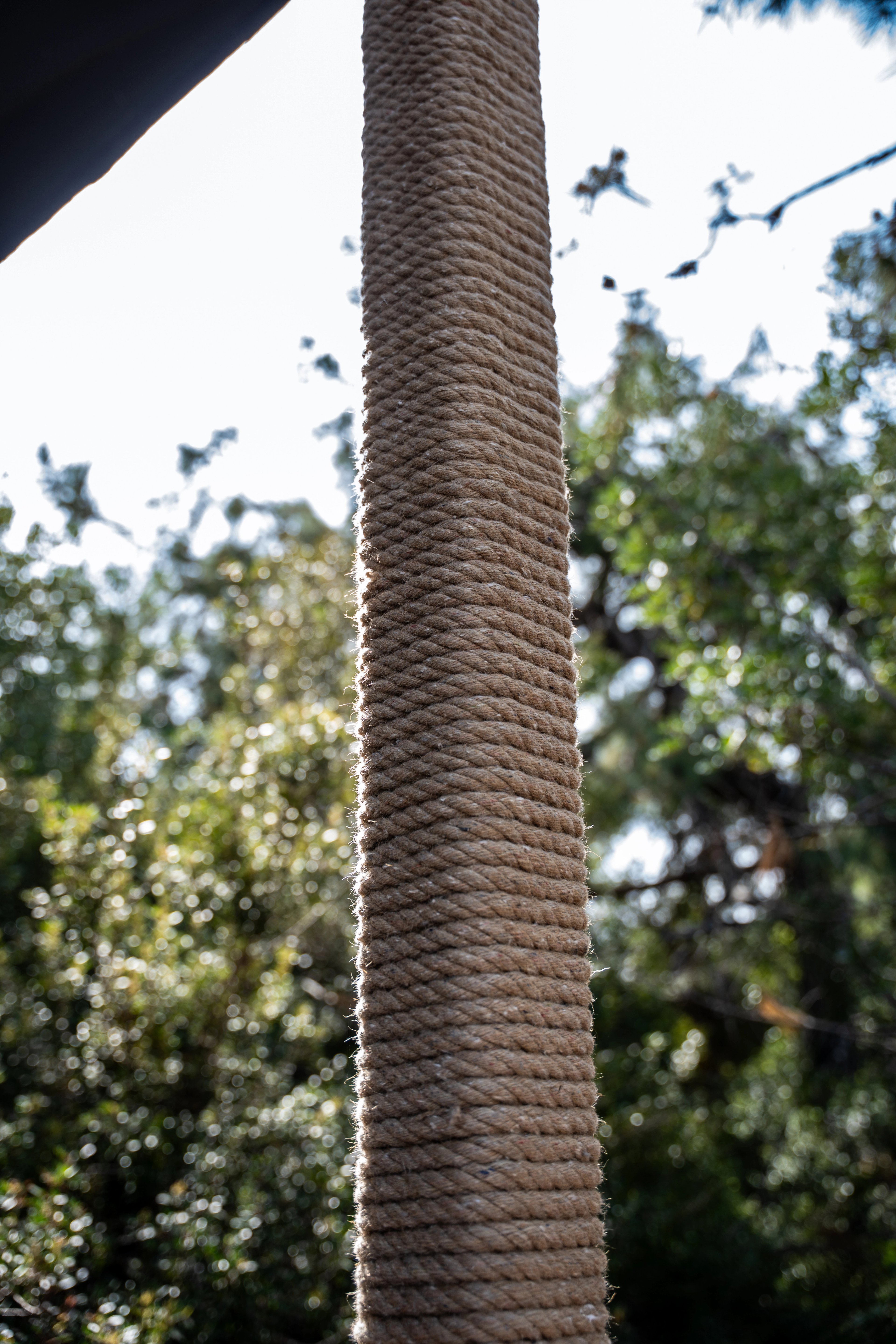 Close view of a tightly rope-wrapped vertical post beneath a beam, with trees behind it at NG Phaselis Bay.