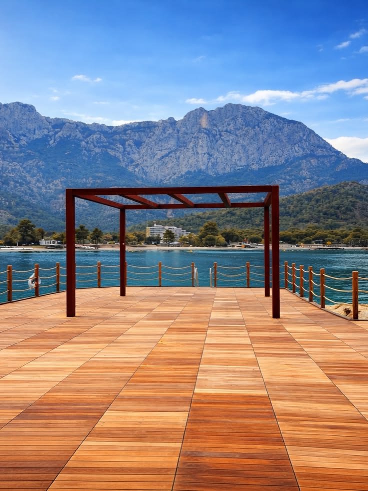 A timber sea platform bordered by rope rails, with a rectangular overhead frame and mountains beyond at NG Phaselis Bay.