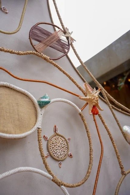Close view of looping rope lines, circular textile details and shells on a pale decorative wall at So Beach.