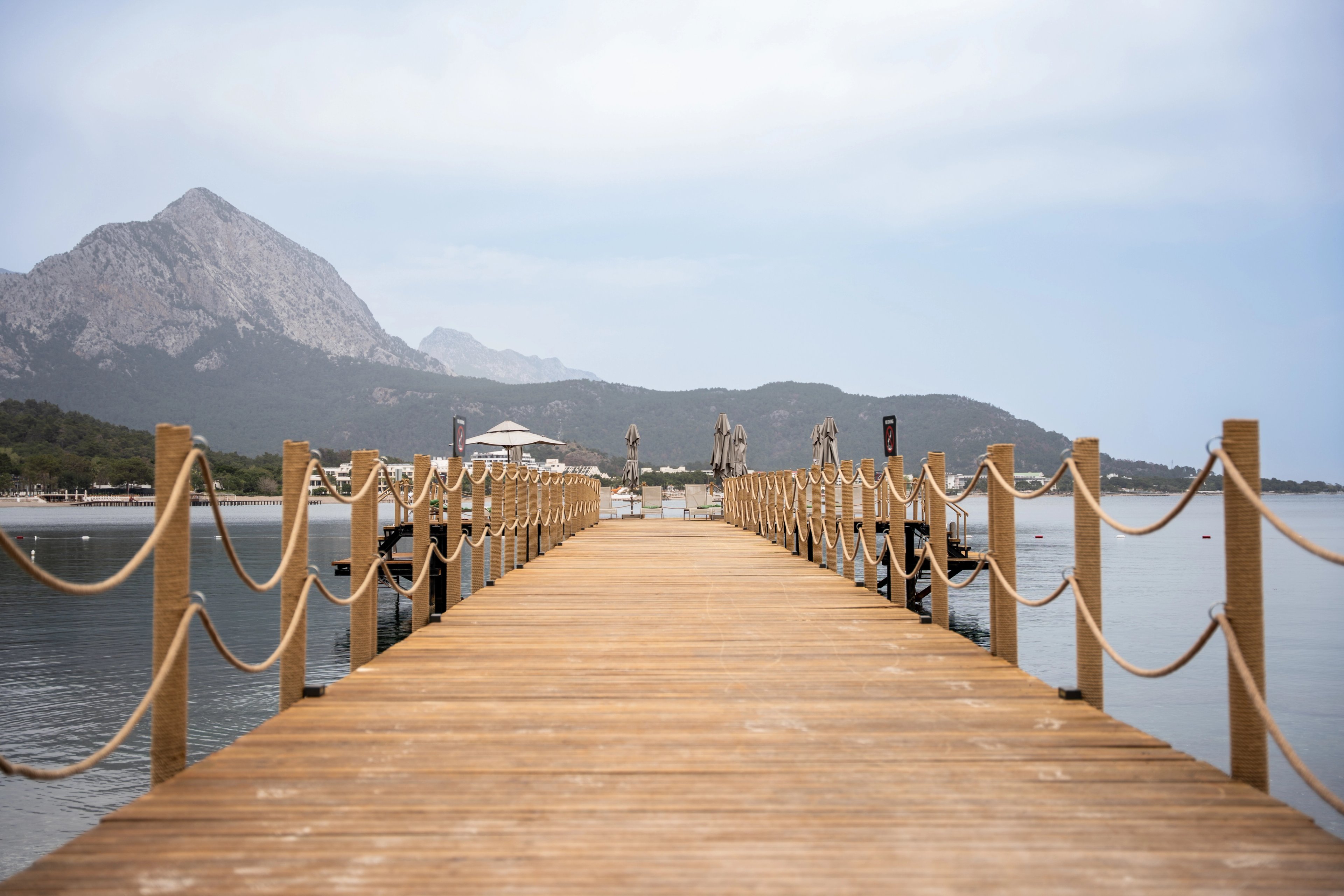 A central view along a timber jetty with looping rope rails and mountains across the water at NG Phaselis Bay.