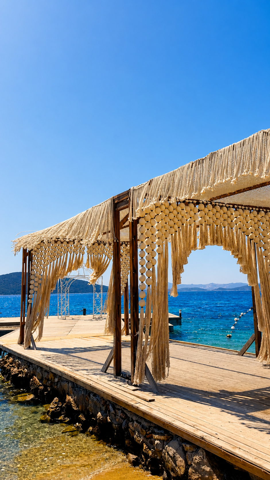 An angled view of fringed canopy frames along a timber platform beside turquoise water at TUI Magic Life Bodrum.