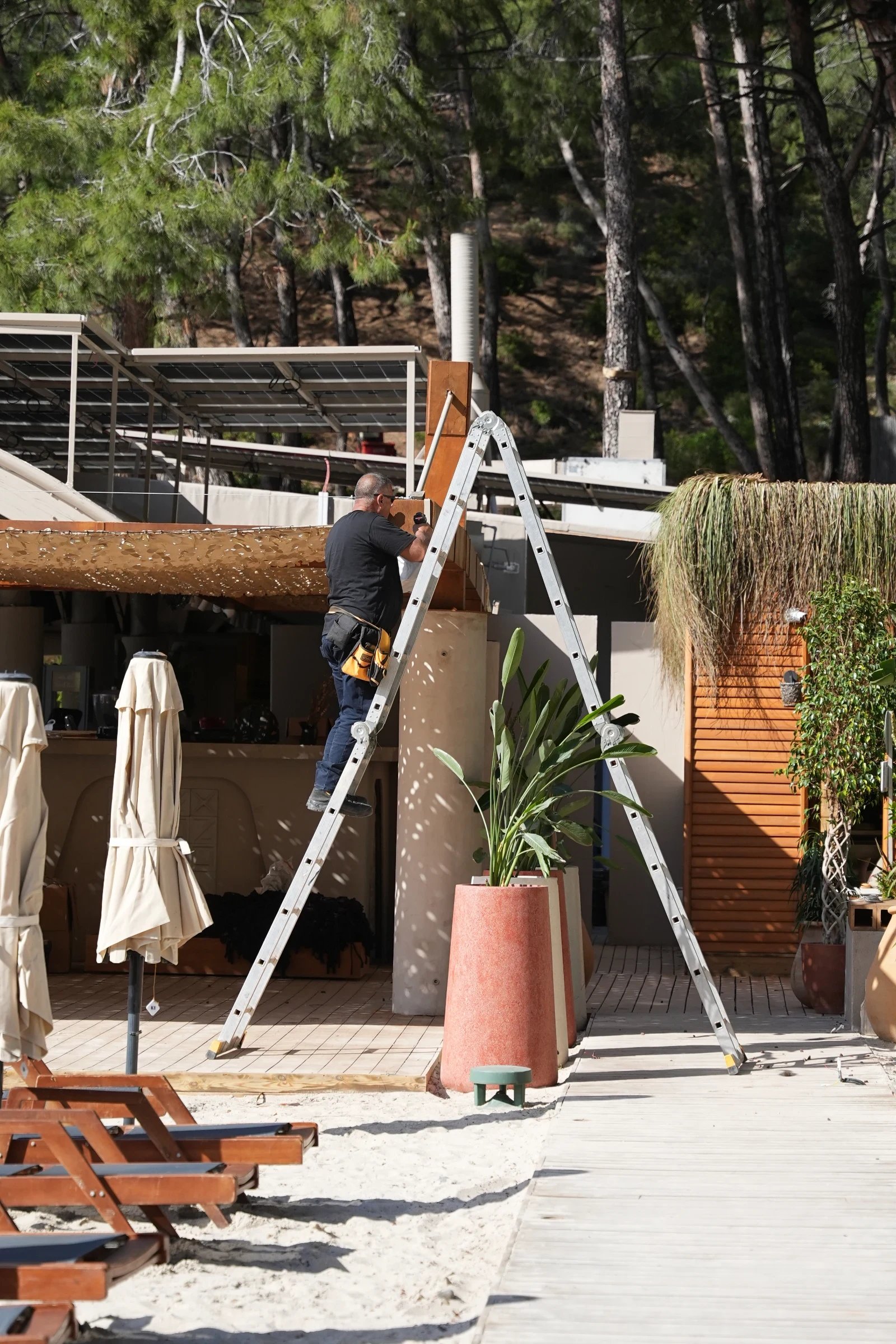 An installer on a ladder working beside an outdoor timber structure.