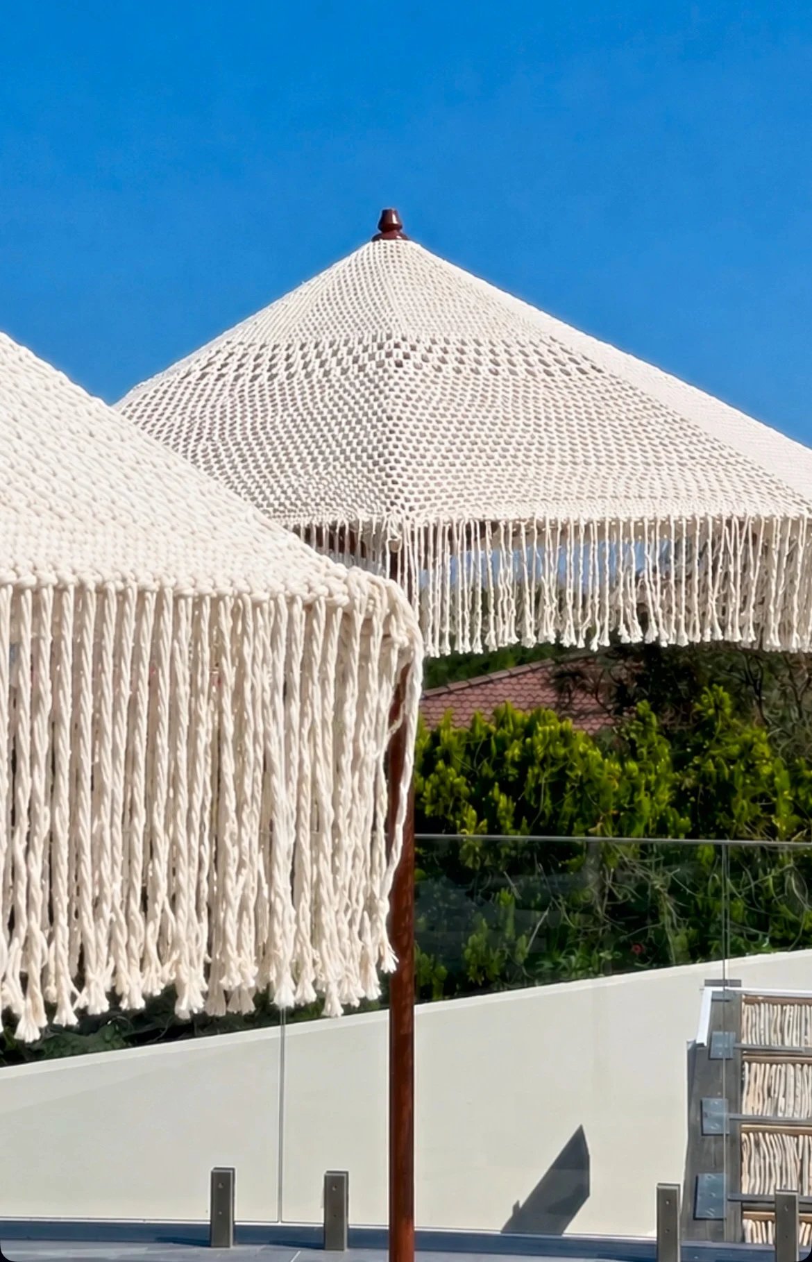 Two Dimare macramé parasols against a clear sky, the open-knotted canopy and long fringe seen close up