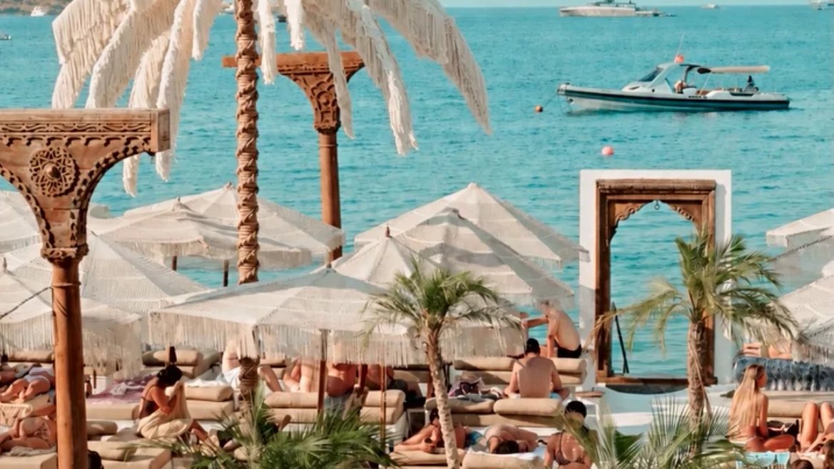 The 8-metre Dimare Palm Tree rising over the sea deck at Reana Beach in Gölköy, Bodrum, with boats on the water beyond
