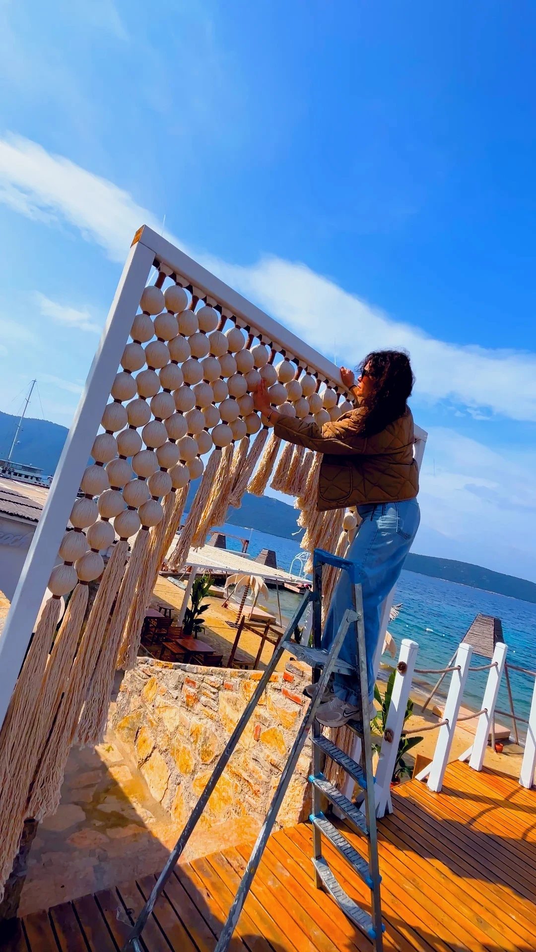 An artisan fitting a panel of rounded woven forms and long fringe to an outdoor frame.