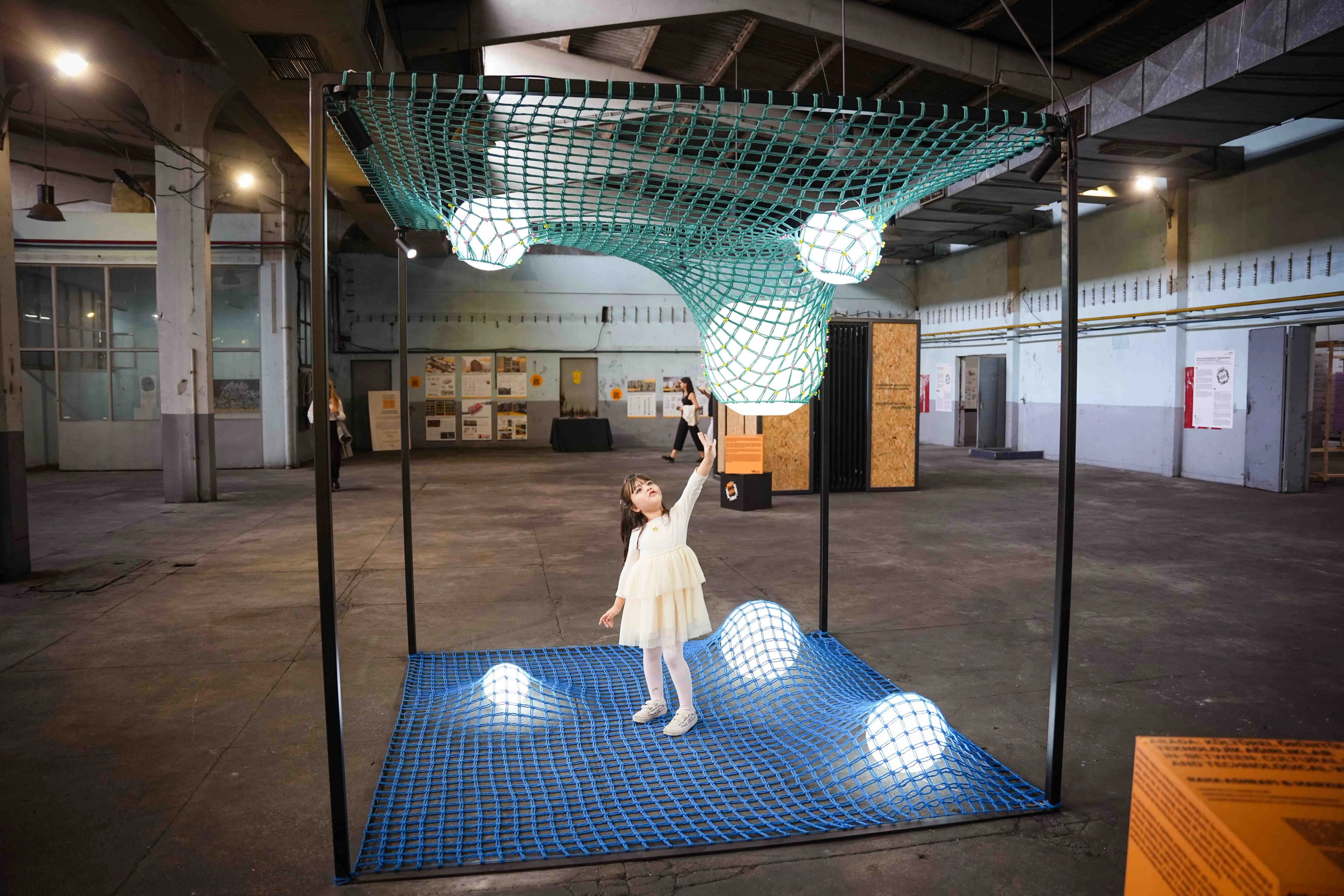 Wide view of a child beneath teal netting and glowing spheres inside a rectangular exhibition frame at IABA 2025.