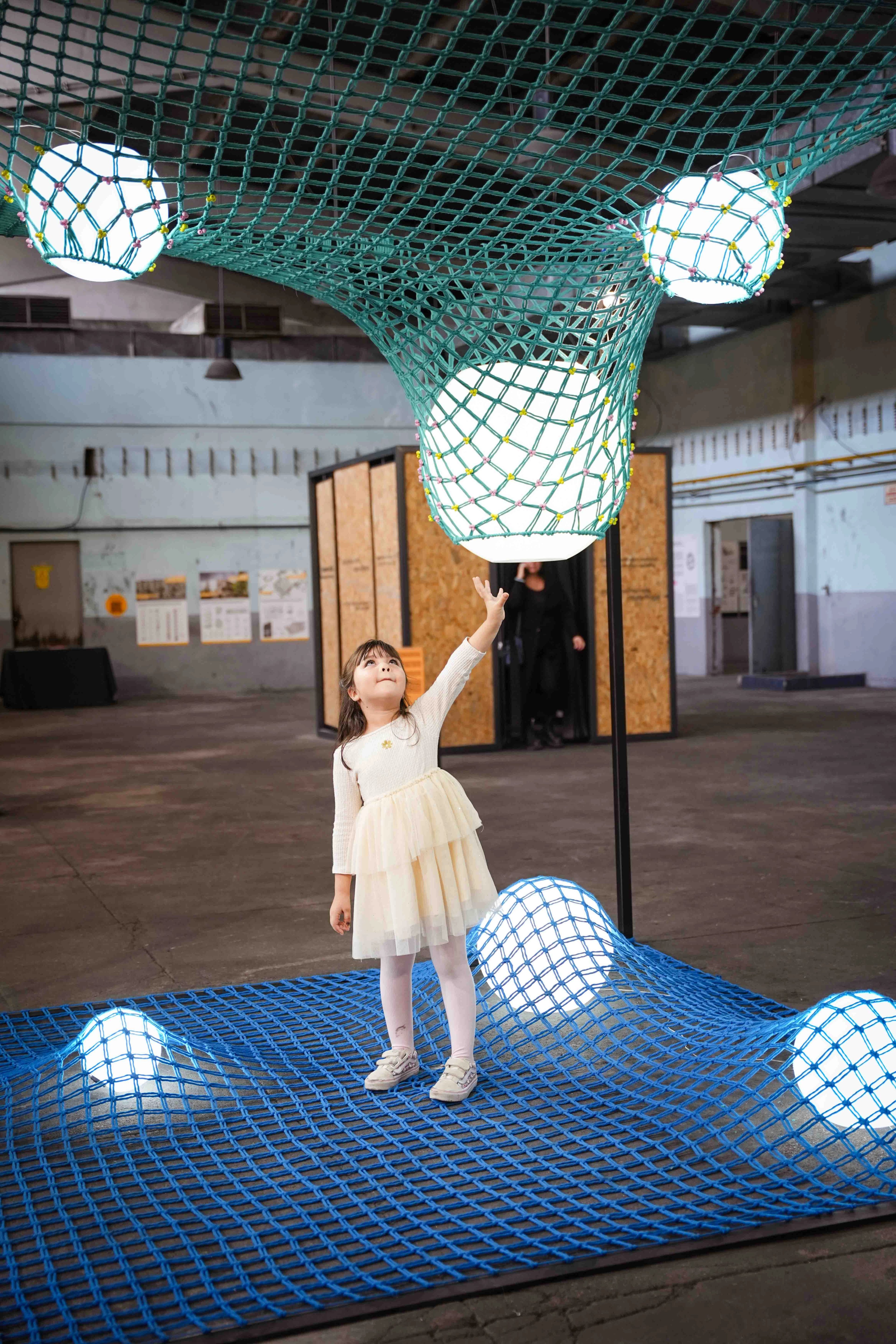 A child reaching toward a glowing sphere held within teal netting above a blue net-covered floor at IABA 2025.