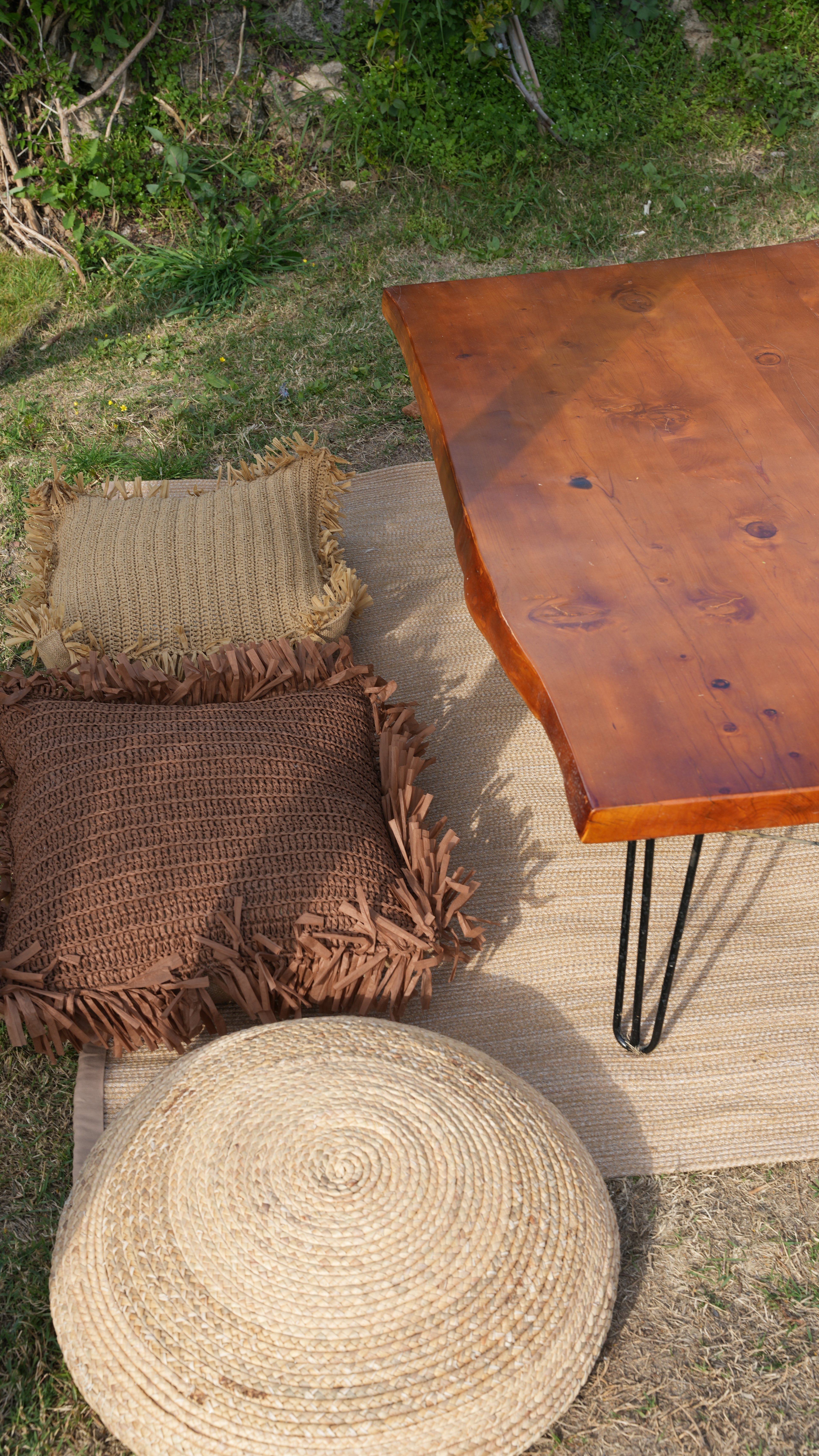 A round woven pouf and fringed brown cushions beside a low timber table at Lucky Monkey Hotel.