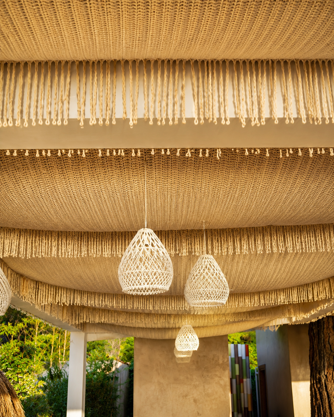 Layers of cream textile ceiling panels with tasseled edges and pendant lights beneath them at So Beach.